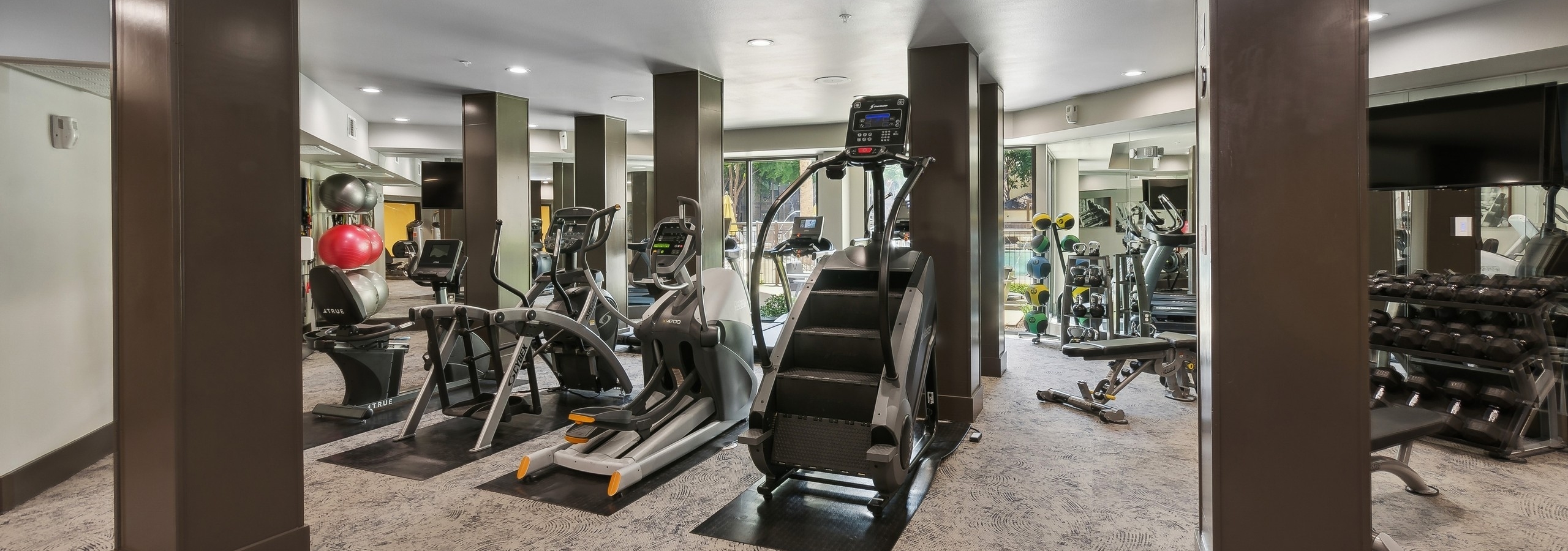 Interior of fitness center at AMLI at the Ballpark apartment building with cardio equipment and dark wood pillars and large windows