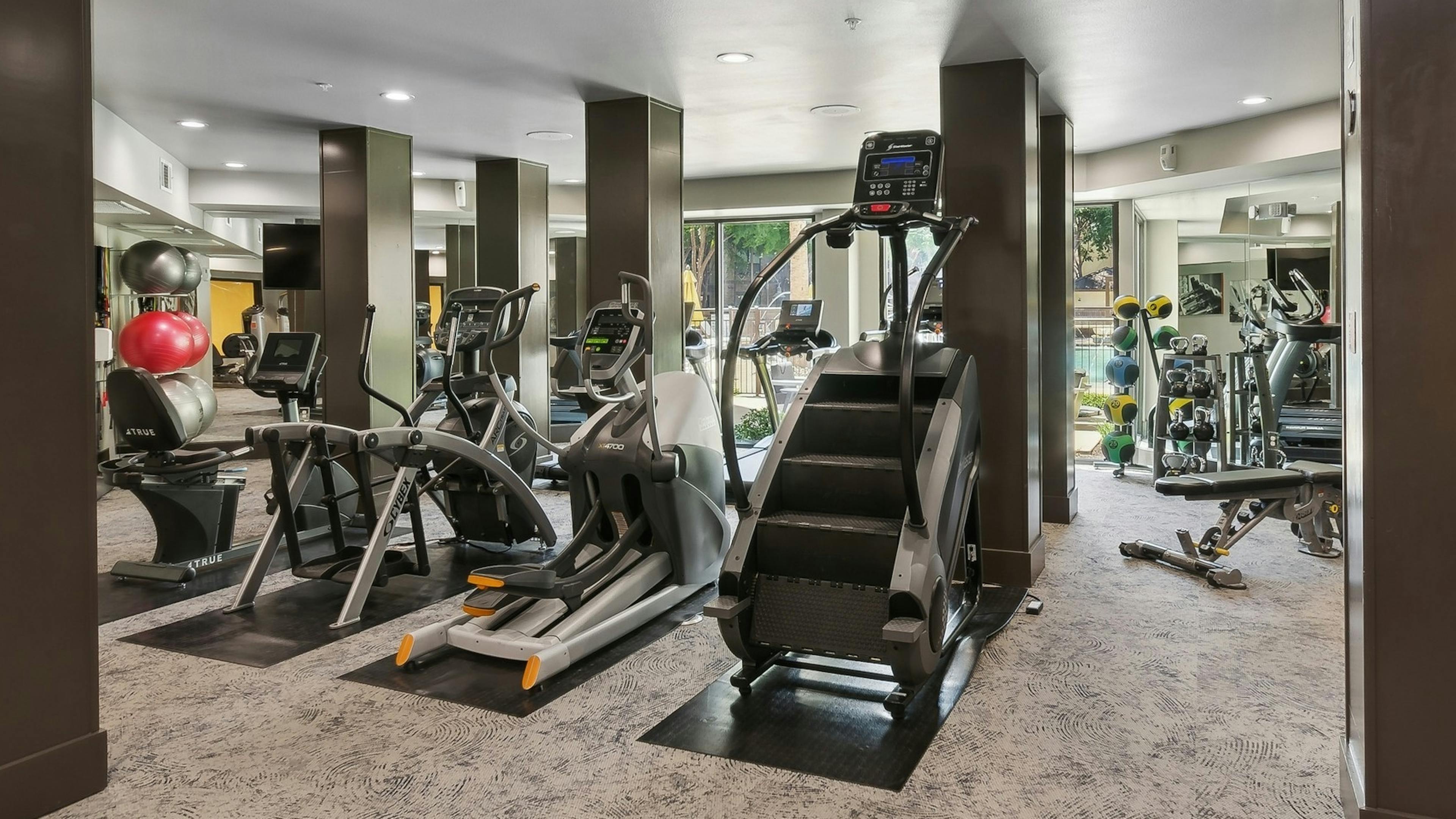 Interior of fitness center at AMLI at the Ballpark apartment building with cardio equipment and dark wood pillars and large windows