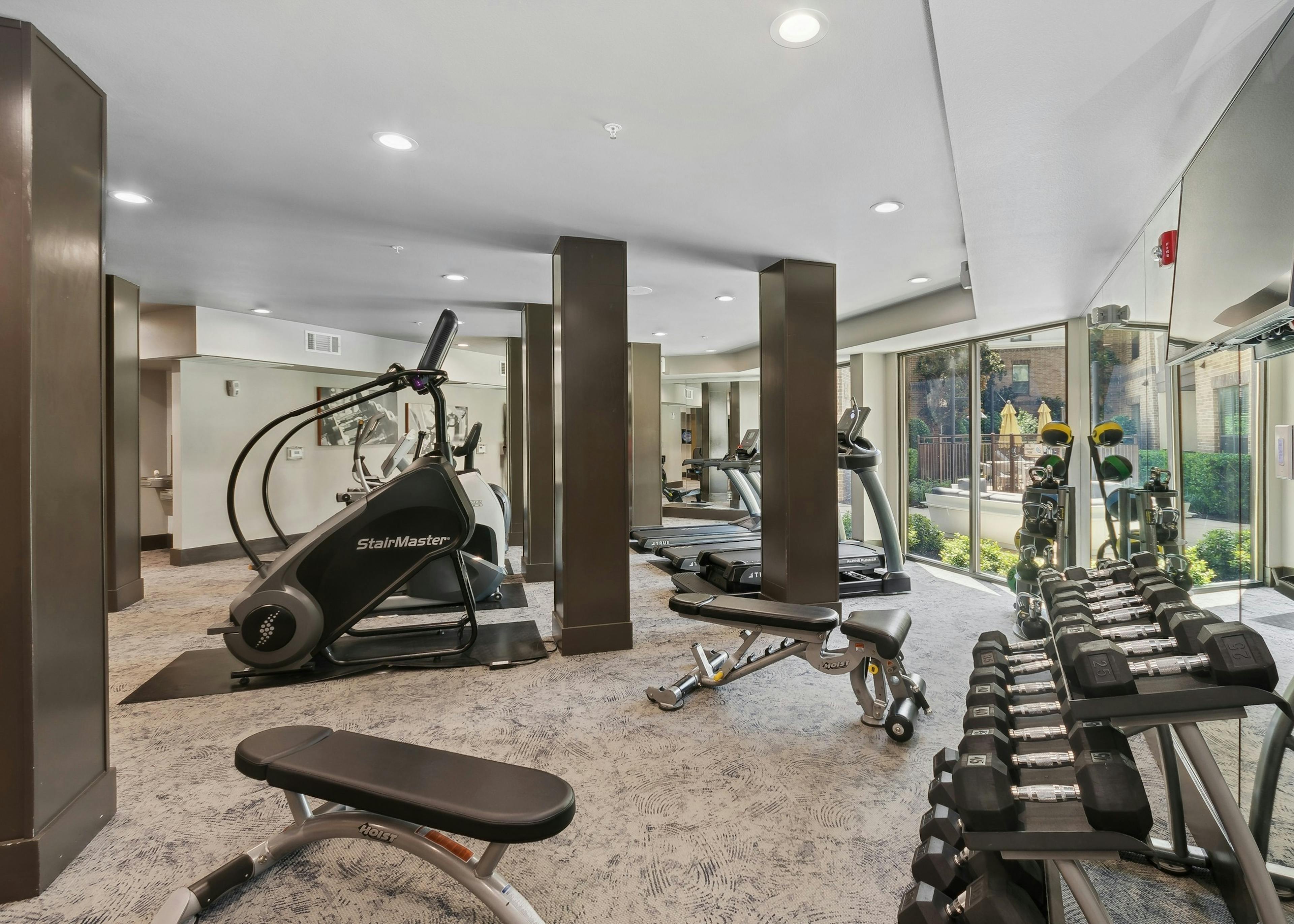 Interior of fitness center at AMLI at the Ballpark apartments with fitness equipment, rack of weights, dark wood pillars and large windows