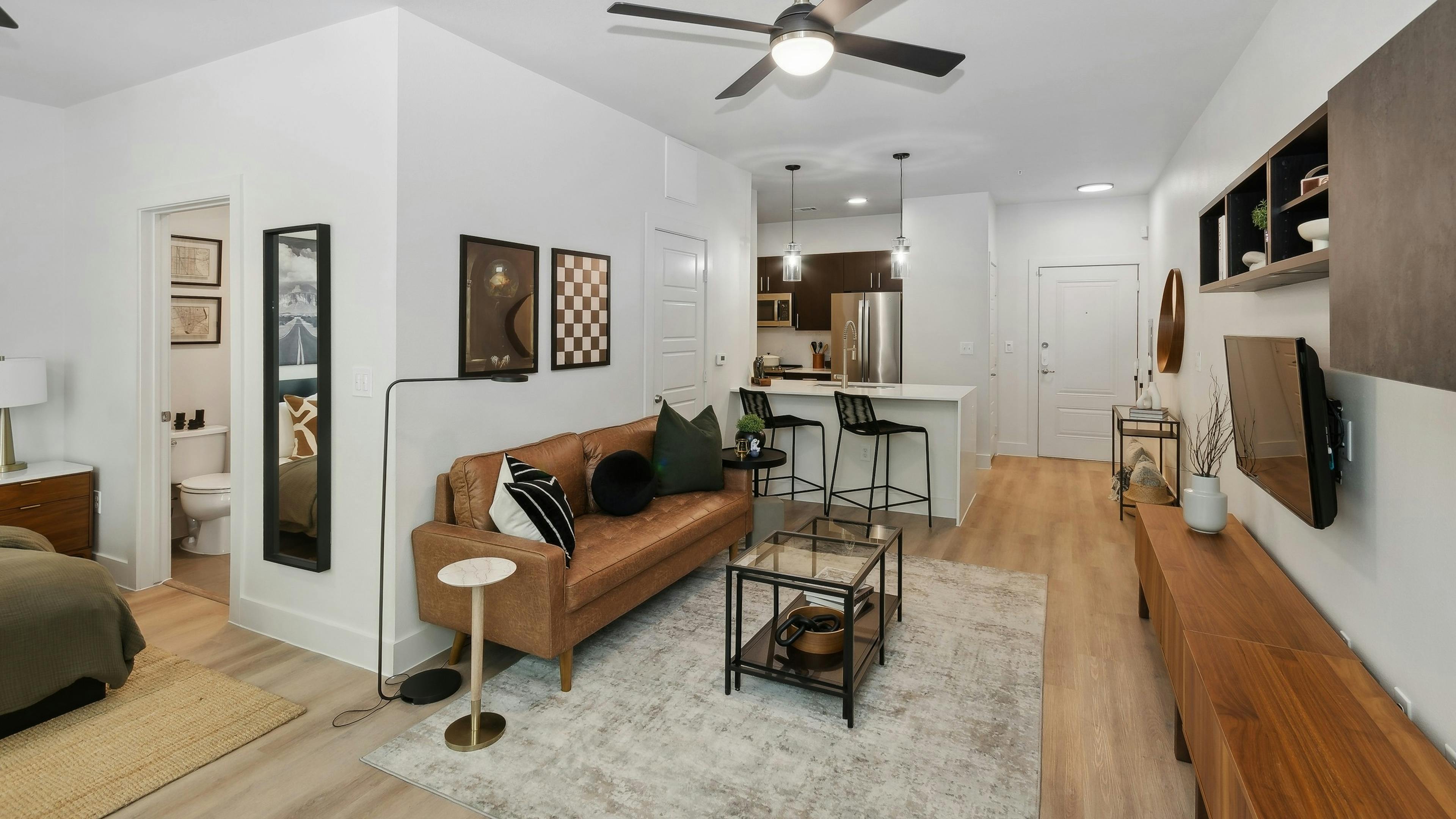 Living area at AMLI at the Ballpark apartment with a leather sofa and glass coffee table looking into an open kitchen with a breakfast bar