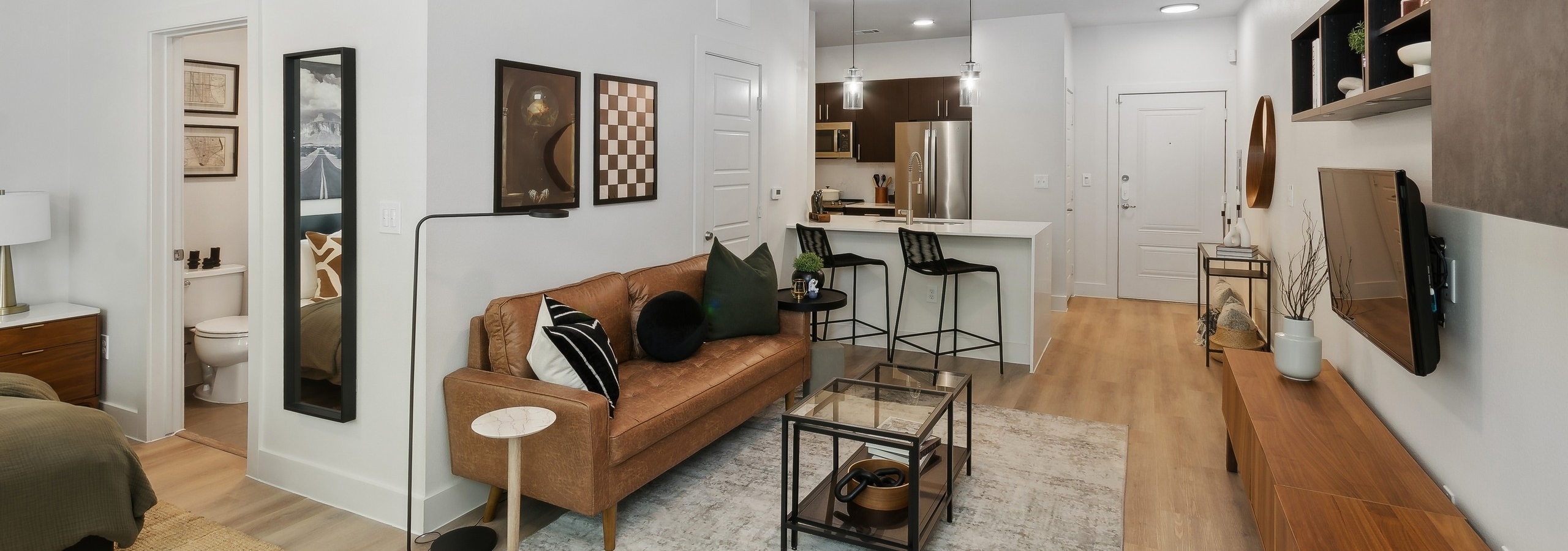 Living area at AMLI at the Ballpark apartment with a leather sofa and glass coffee table looking into an open kitchen with a breakfast bar