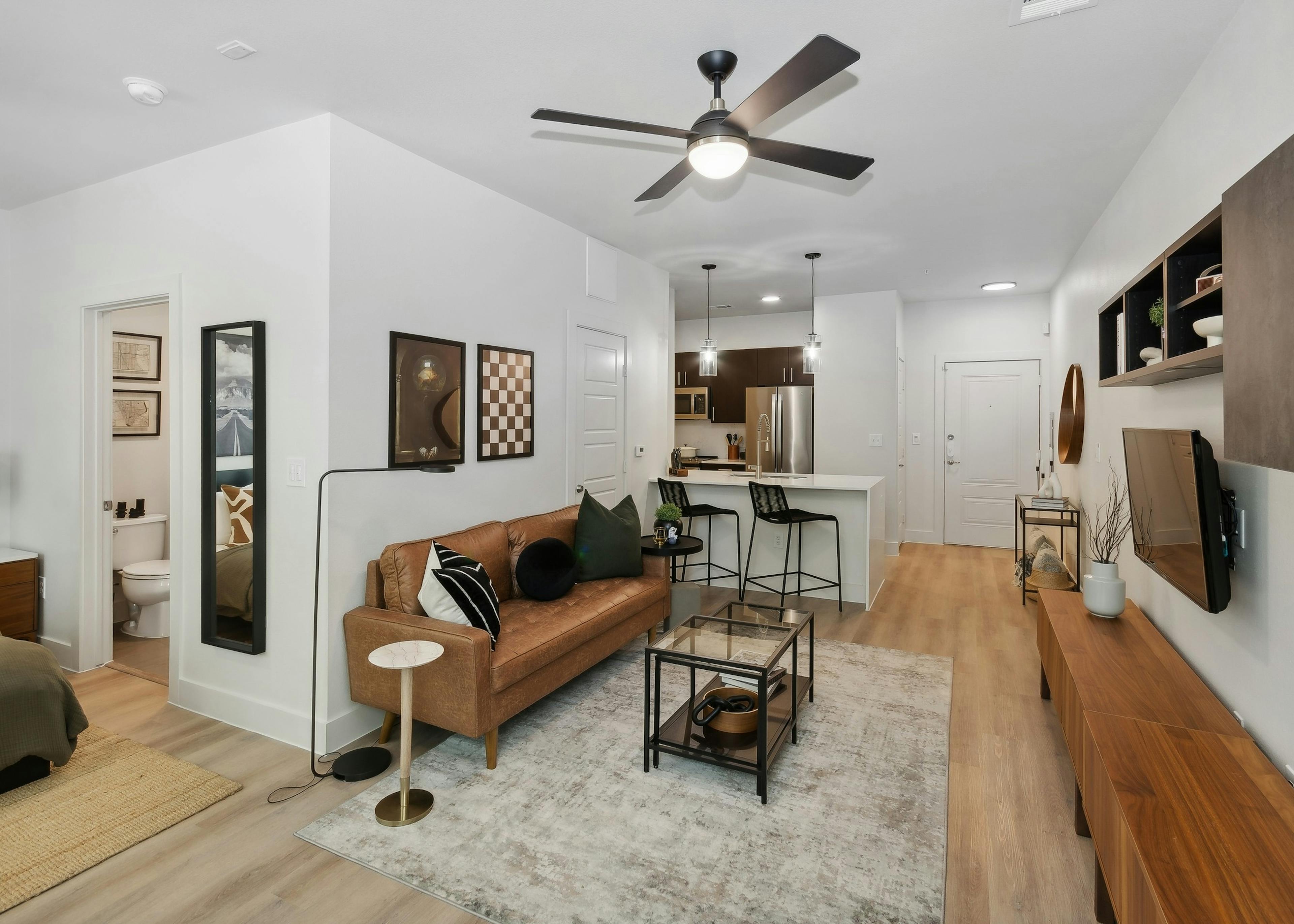 Living area at AMLI at the Ballpark apartment with a leather sofa and glass coffee table looking into an open kitchen with a breakfast bar