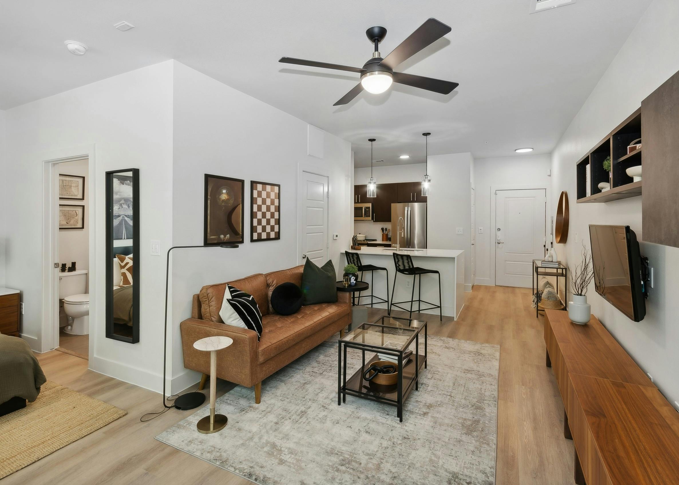 Living area at AMLI at the Ballpark apartment with a leather sofa and glass coffee table looking into an open kitchen with a breakfast bar