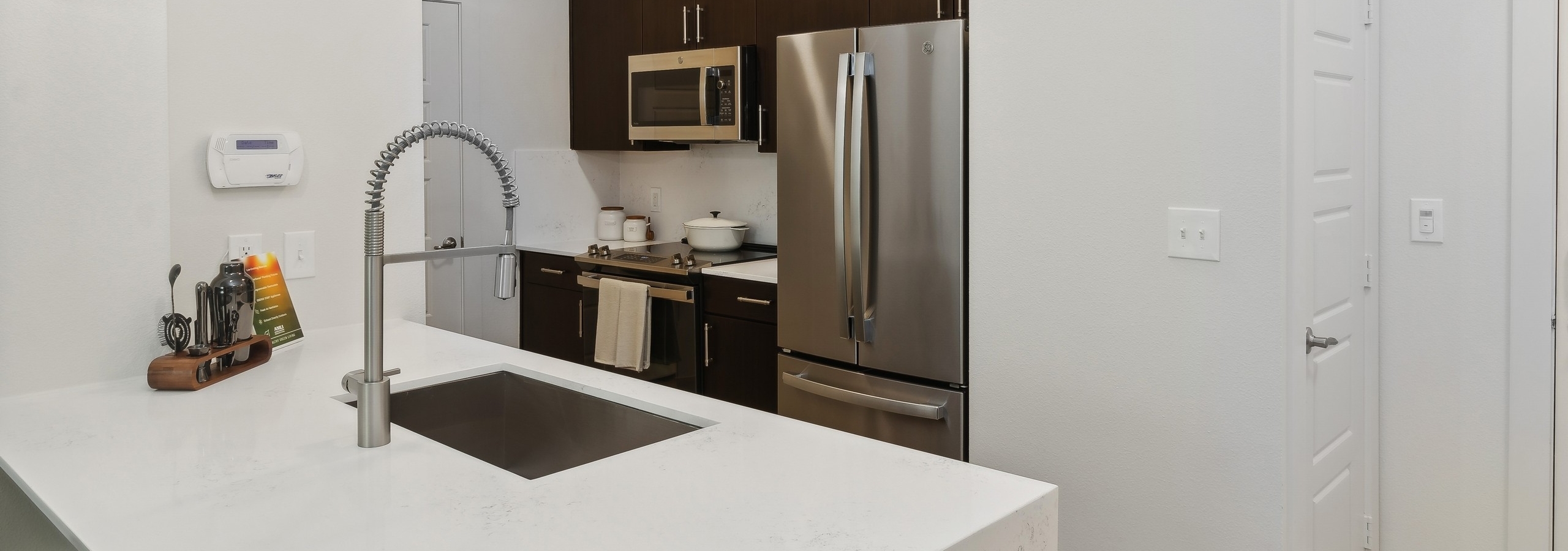 Kitchen at AMLI at the Ballpark with white walls and countertops, curved faucet, stainless steel appliances and dark brown cabinets