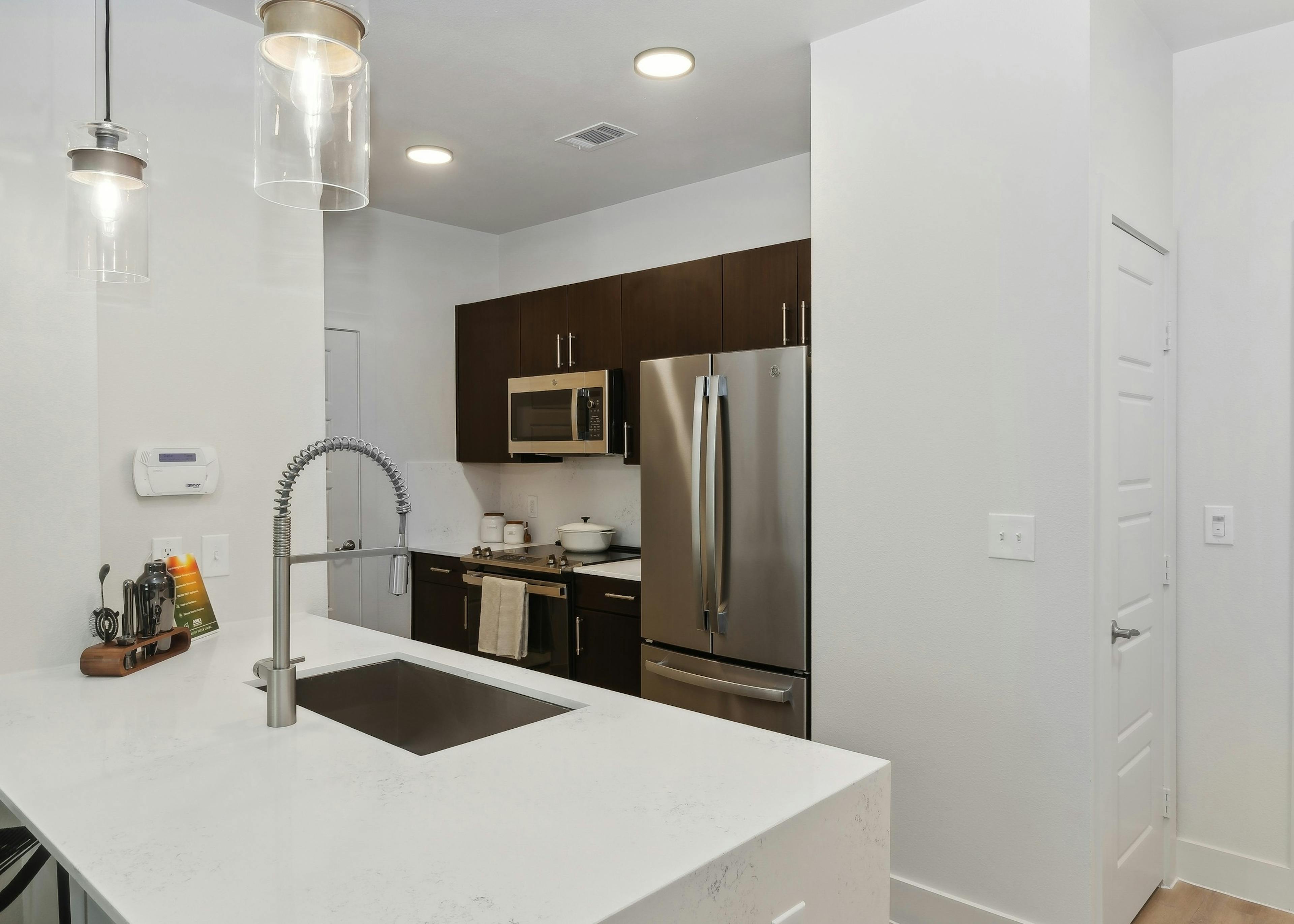 Kitchen at AMLI at the Ballpark with white walls and countertops, curved faucet, stainless steel appliances and dark brown cabinets