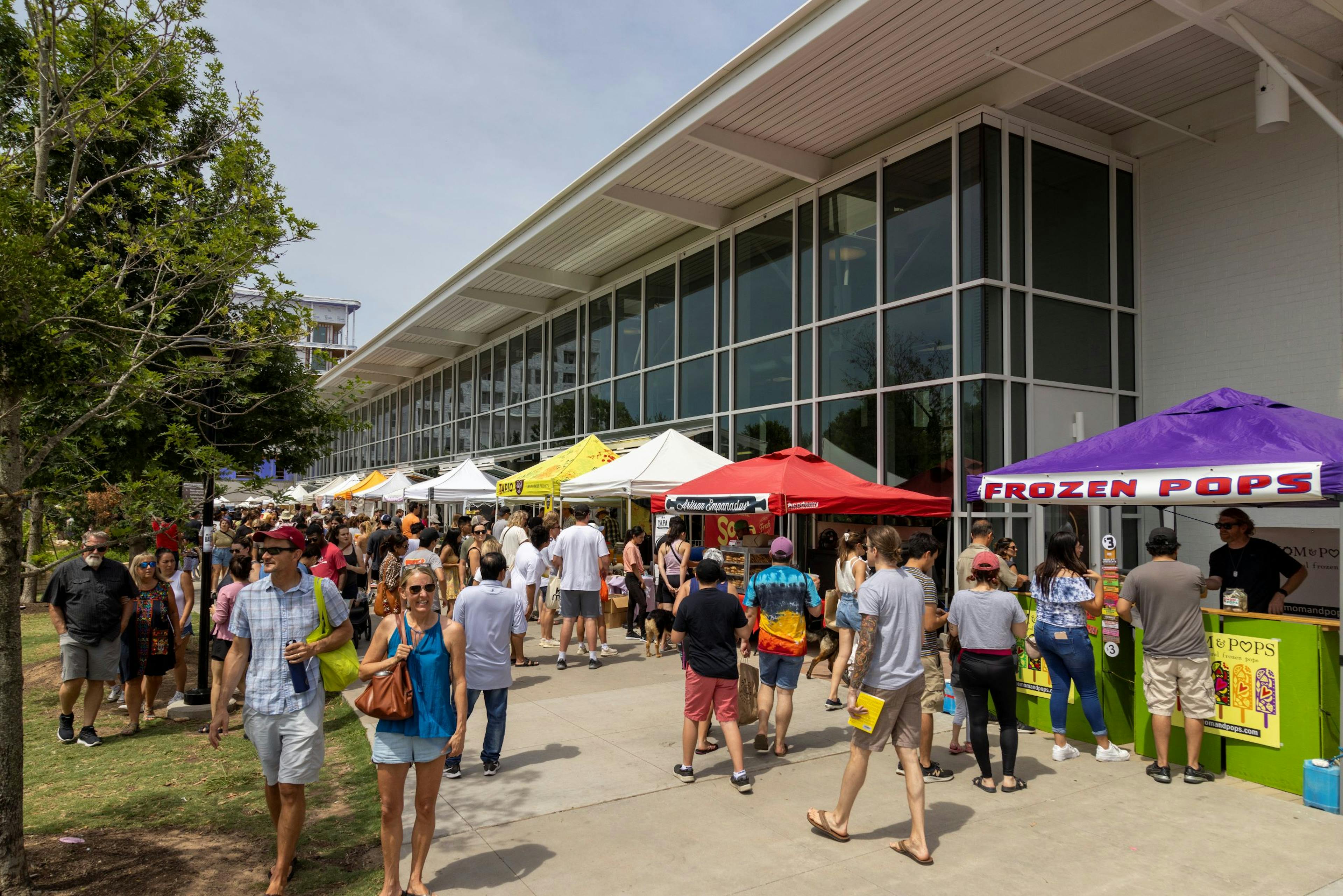 Farmers market in Mueller filled with colorful tents and people walking along a building and shopping