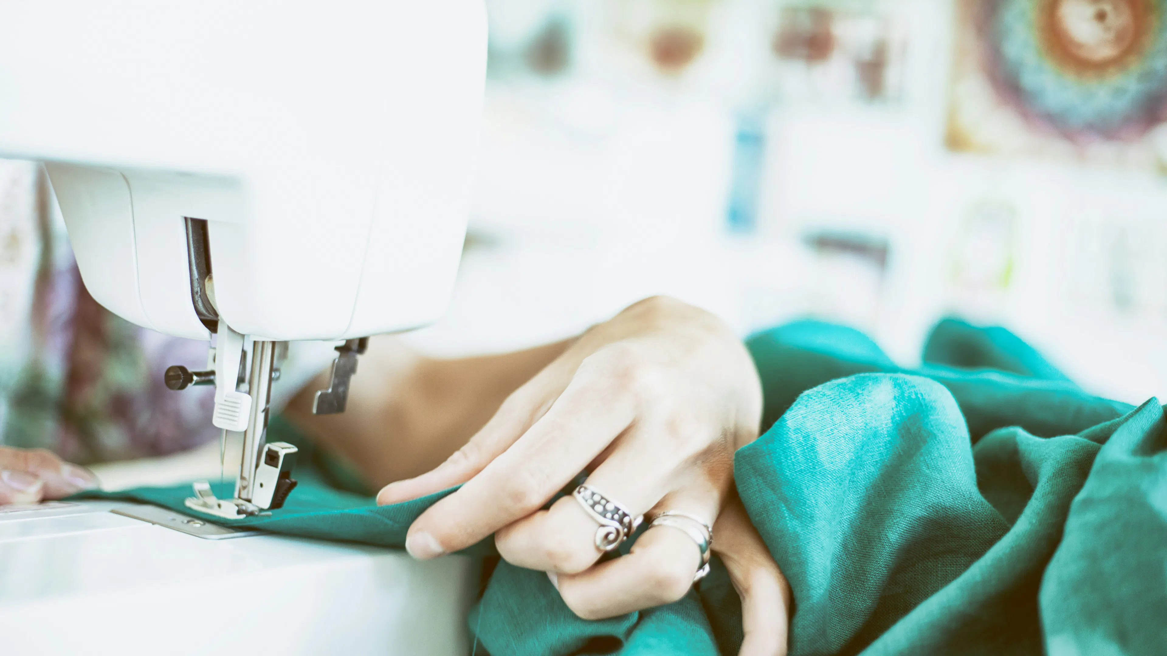 A womans hand guiding some green fabric through a sewing machine 