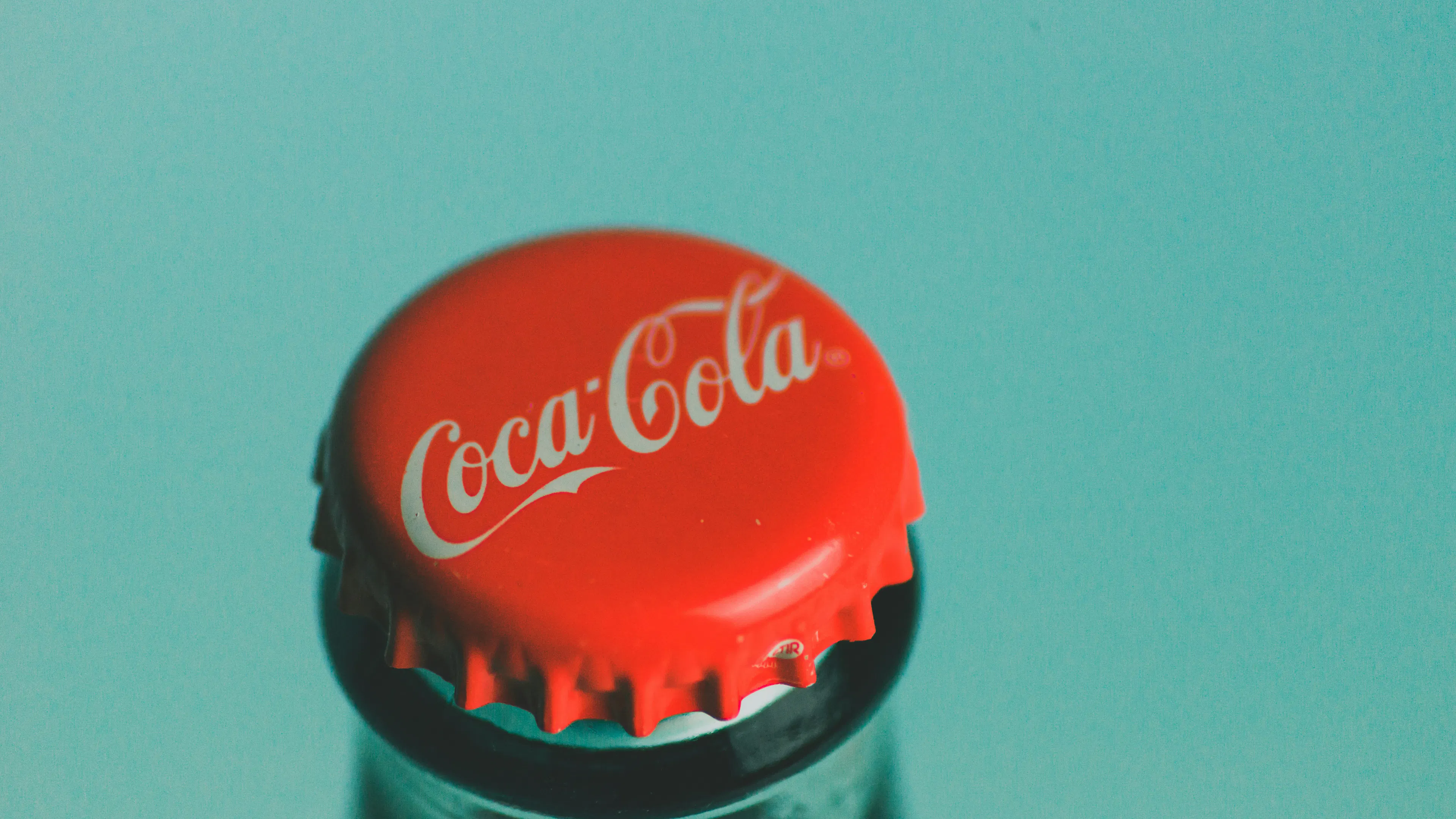 A close up of a bottle cap on a glass bottle of Coca-Cola