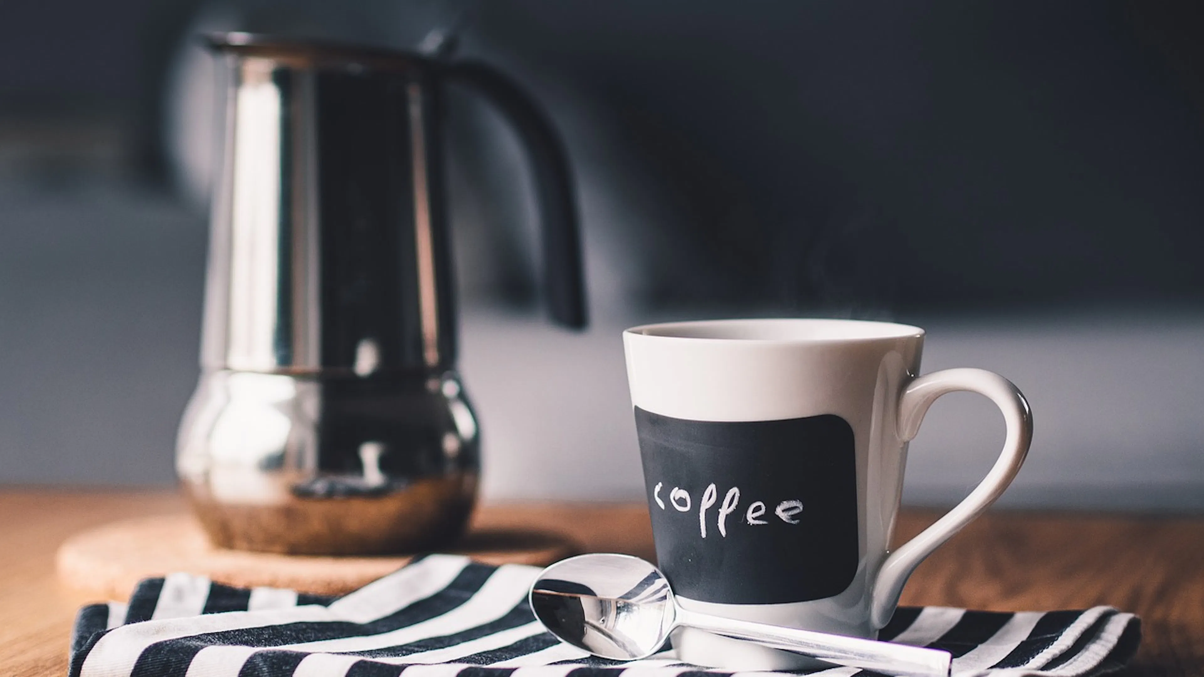 metal coffee pot with coffee mug and white and black stripe towel