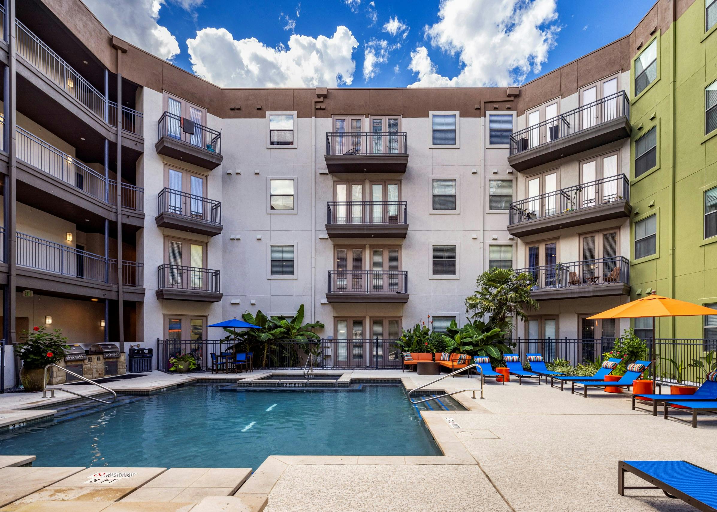 AMLI 300 apartments central courtyard with a swimming pool surrounded by blue lounge chairs and a grill station below building balconies