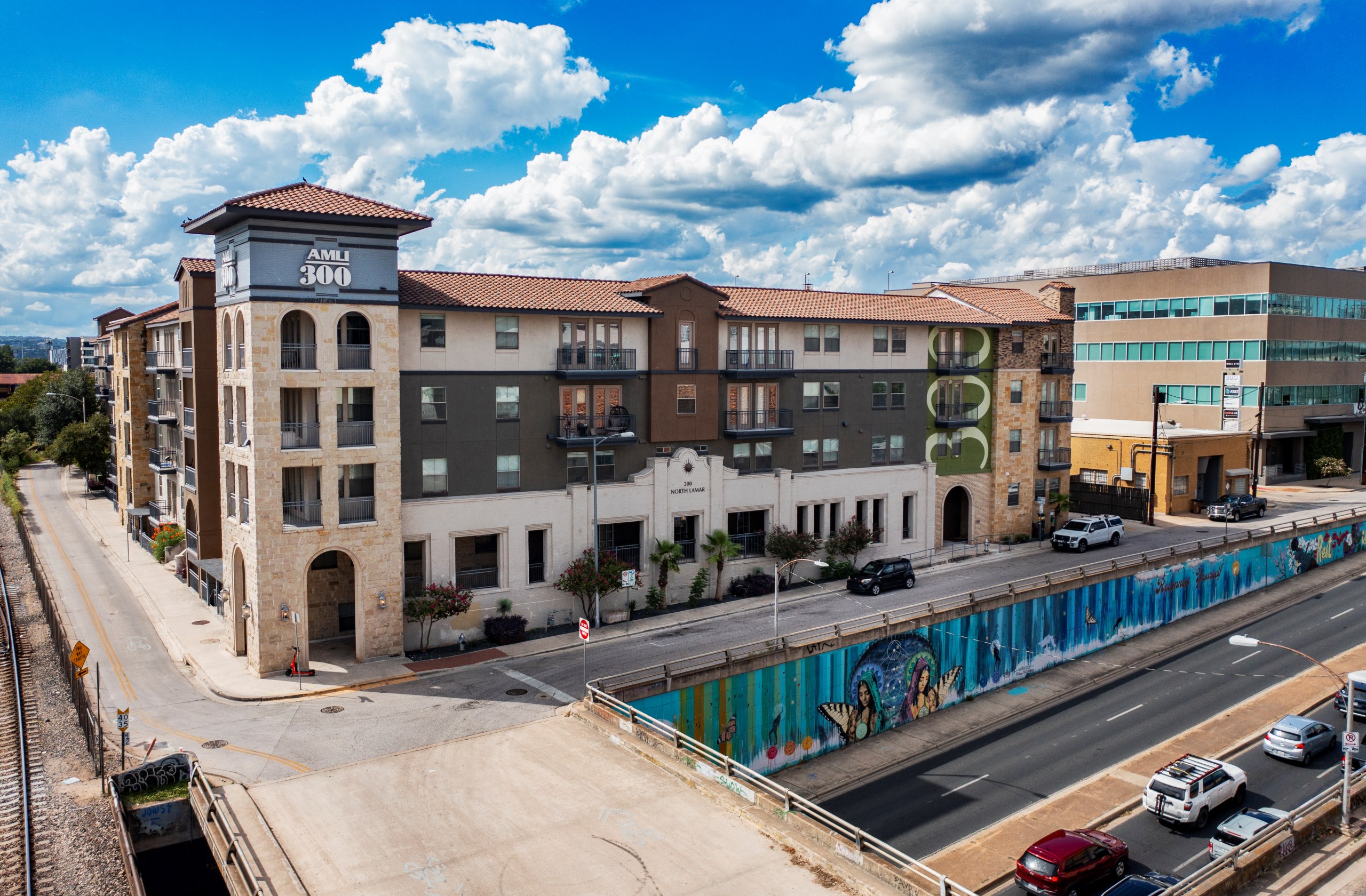 AMLI 300 apartment building featuring a blend of stone and dark siding accents above a mural decorated underpass