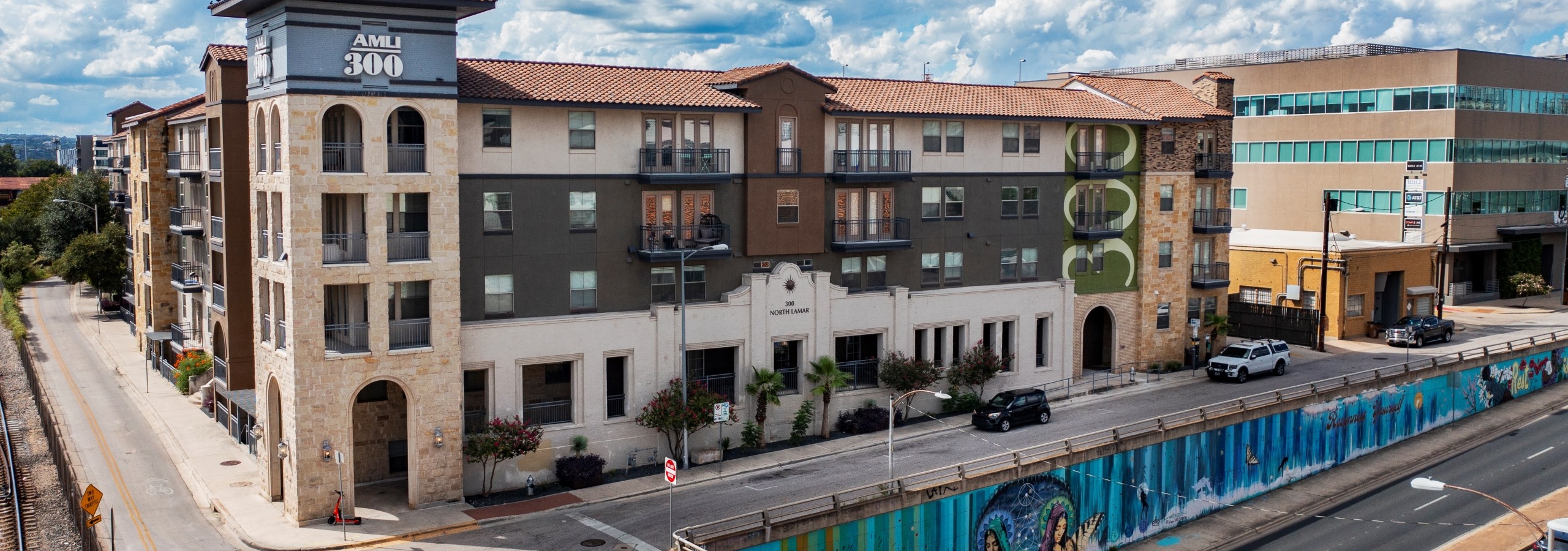 AMLI 300 apartment building featuring a blend of stone and dark siding accents above a mural decorated underpass
