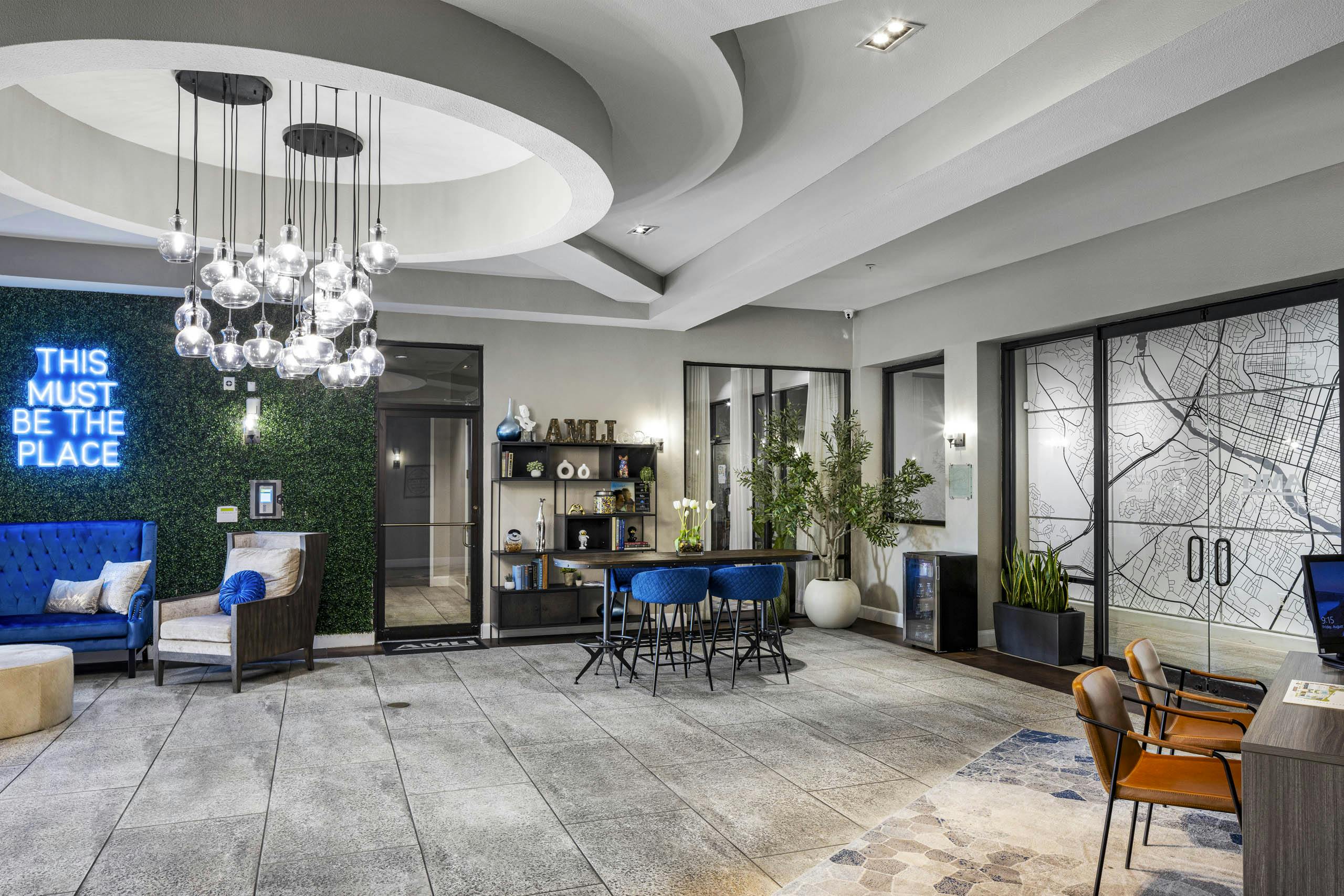 AMLI Eastside apartments leasing office featuring a mix of bright blue décor and a neon sign reading this must be the place on a plant wall
