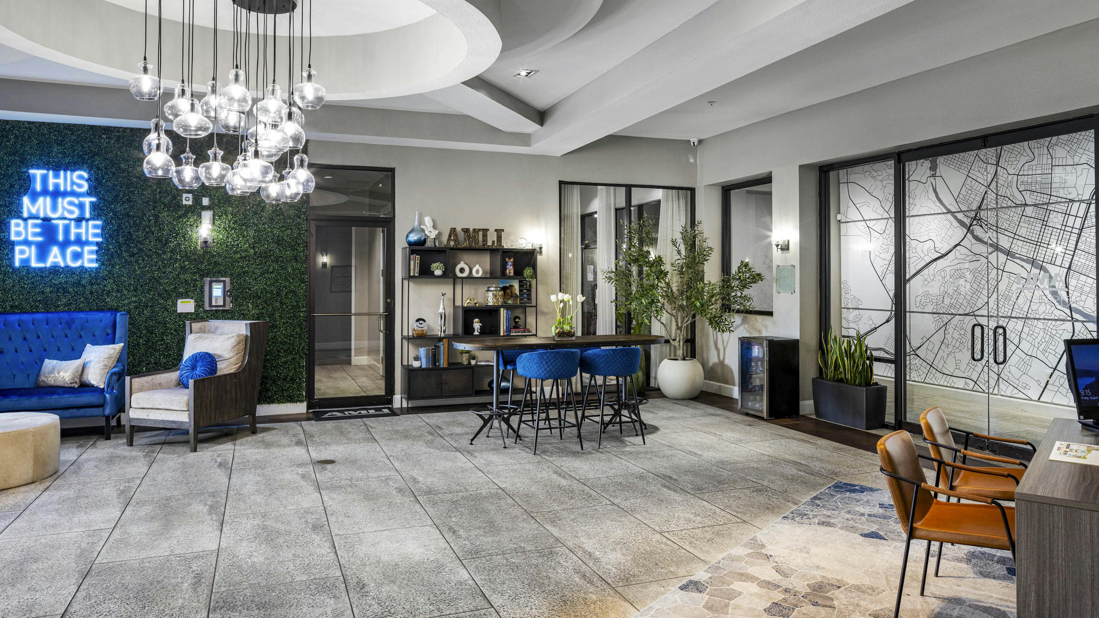 AMLI Eastside apartments leasing office featuring a mix of bright blue décor and a neon sign reading this must be the place on a plant wall