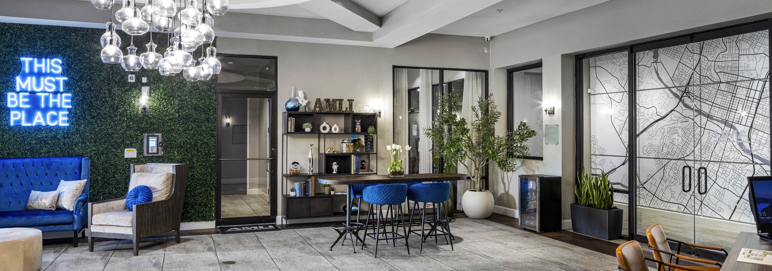 AMLI Eastside apartments leasing office featuring a mix of bright blue décor and a neon sign reading this must be the place on a plant wall