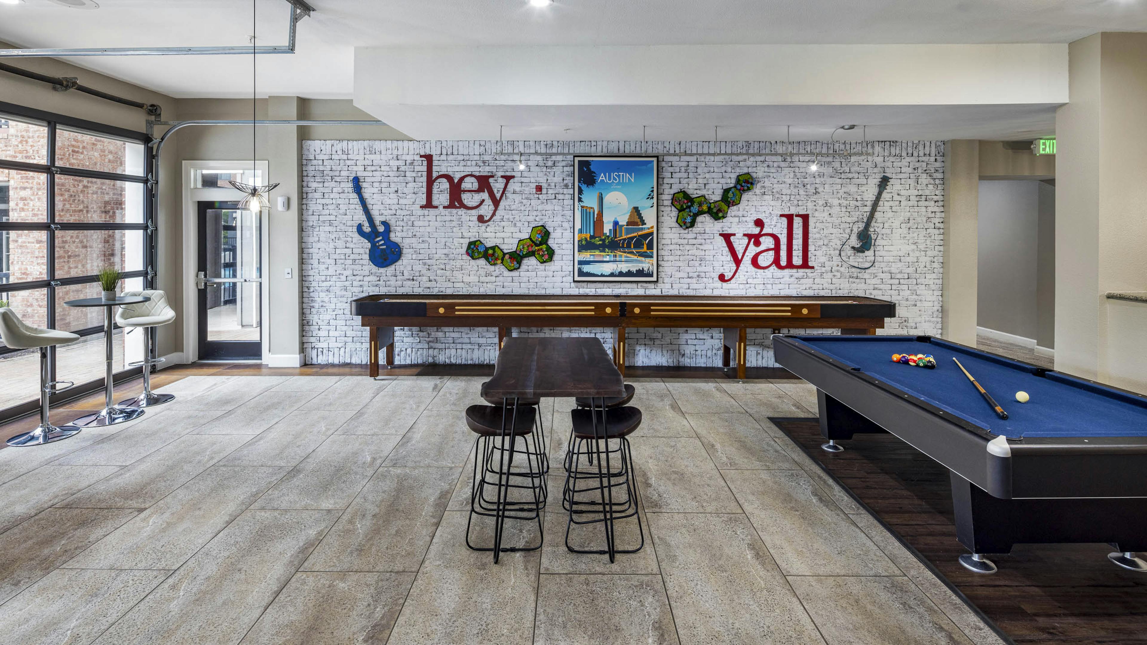AMLI Eastside apartments resident lounge with a pool table, shuffleboard and a white brick wall with guitars and a poster of Austin