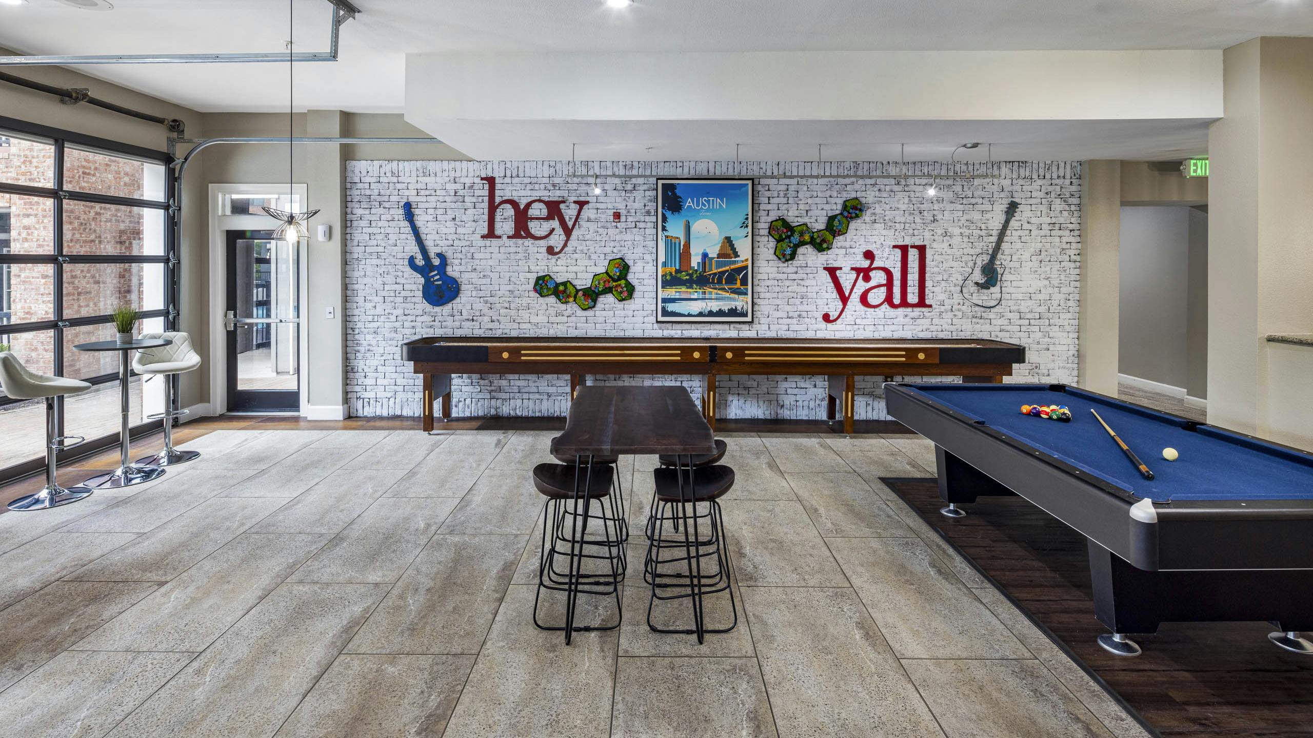 AMLI Eastside apartments resident lounge with a pool table, shuffleboard and a white brick wall with guitars and a poster of Austin
