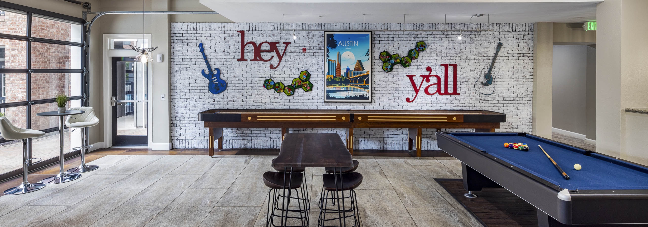 AMLI Eastside apartments resident lounge with a pool table, shuffleboard and a white brick wall with guitars and a poster of Austin