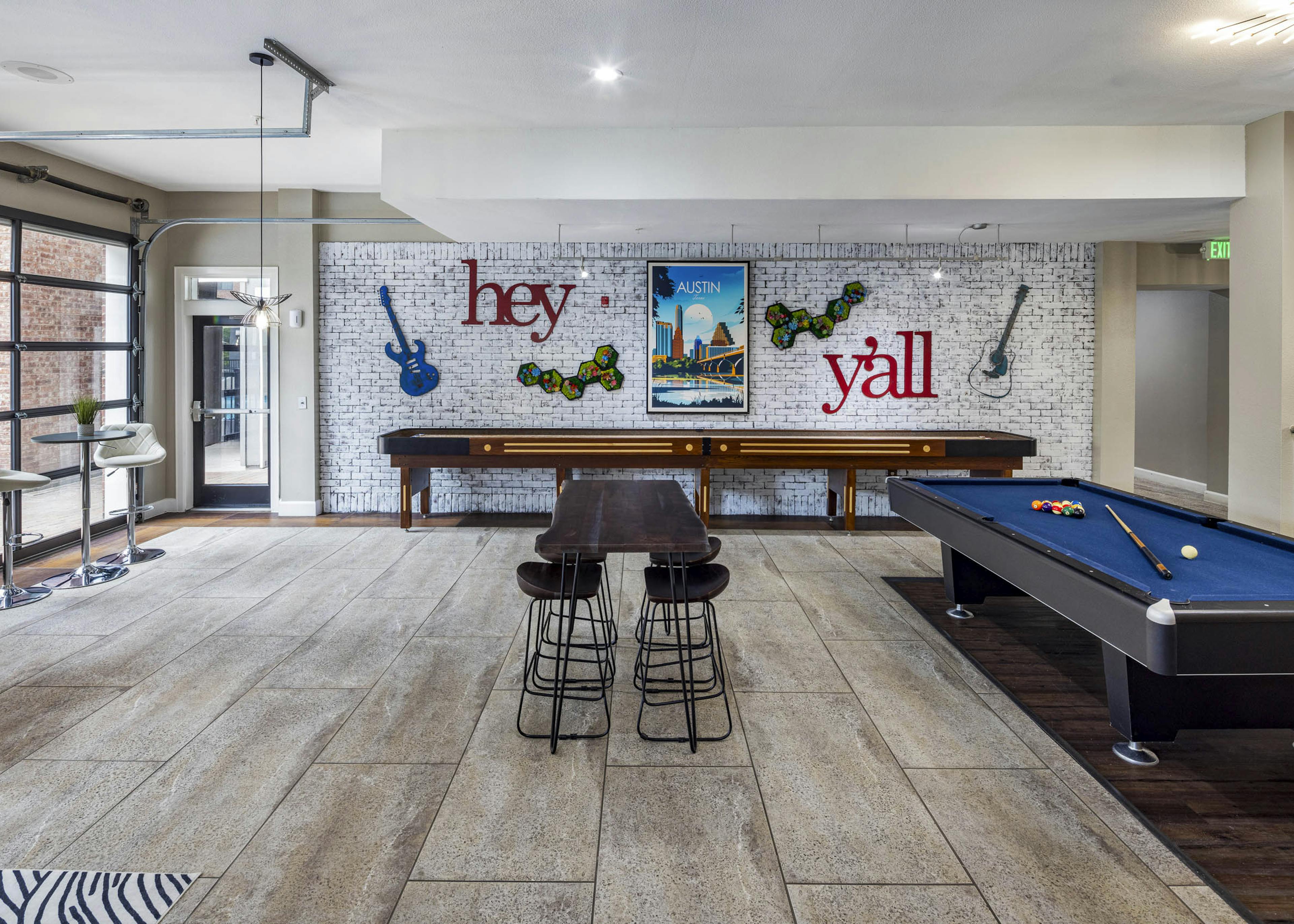 AMLI Eastside apartments resident lounge with a pool table, shuffleboard and a white brick wall with guitars and a poster of Austin