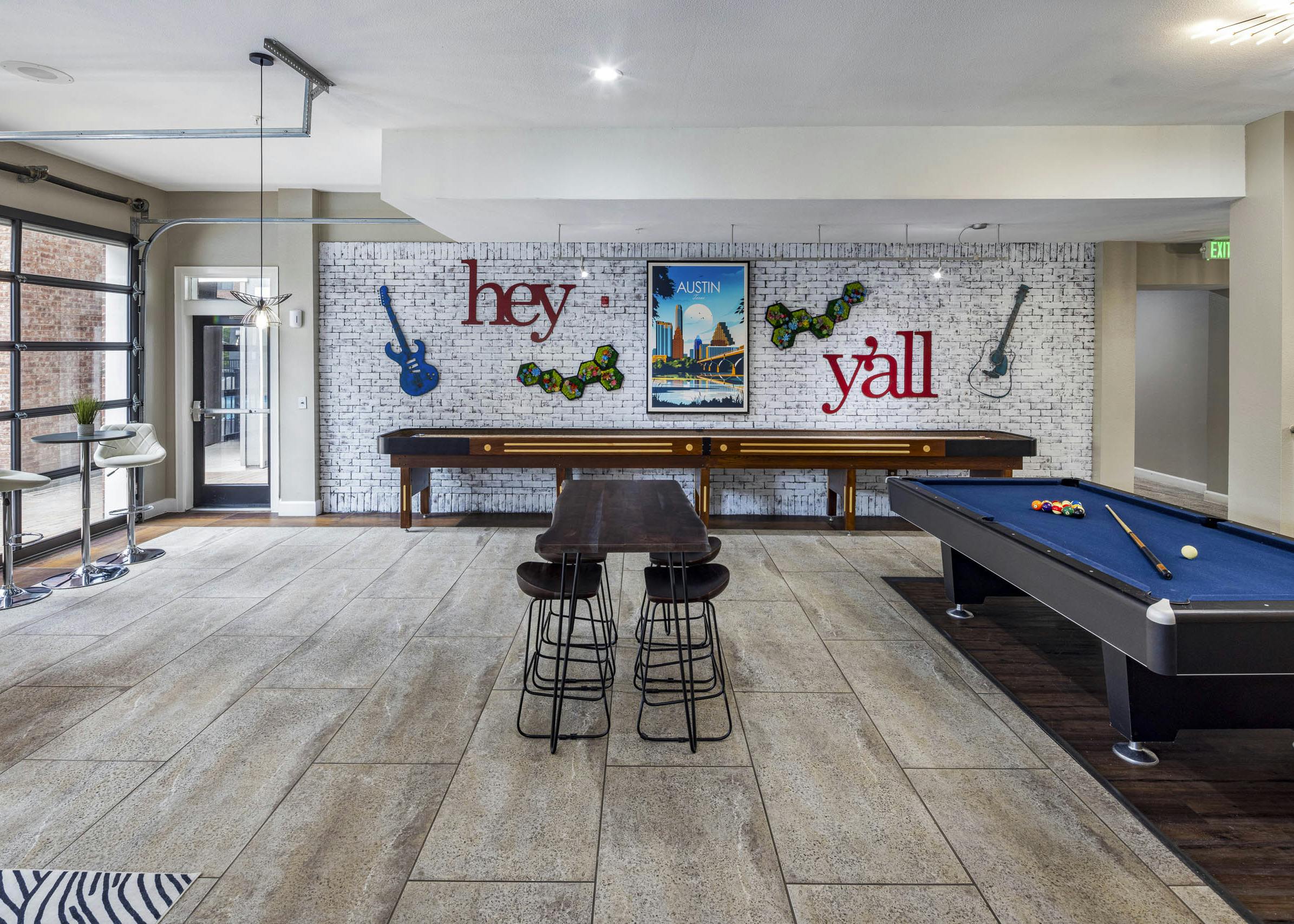 AMLI Eastside apartments resident lounge with a pool table, shuffleboard and a white brick wall with guitars and a poster of Austin