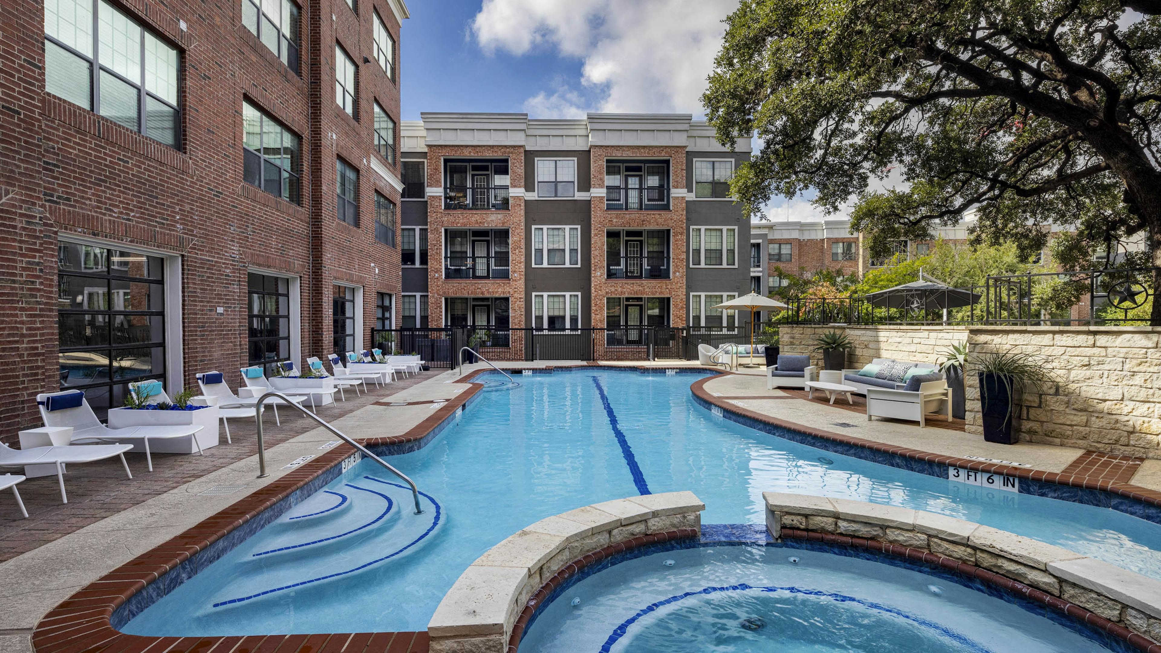 AMLI Eastside apartments swimming pool with a connected circular hot tub surrounded by white lounge chairs and brick buildings
