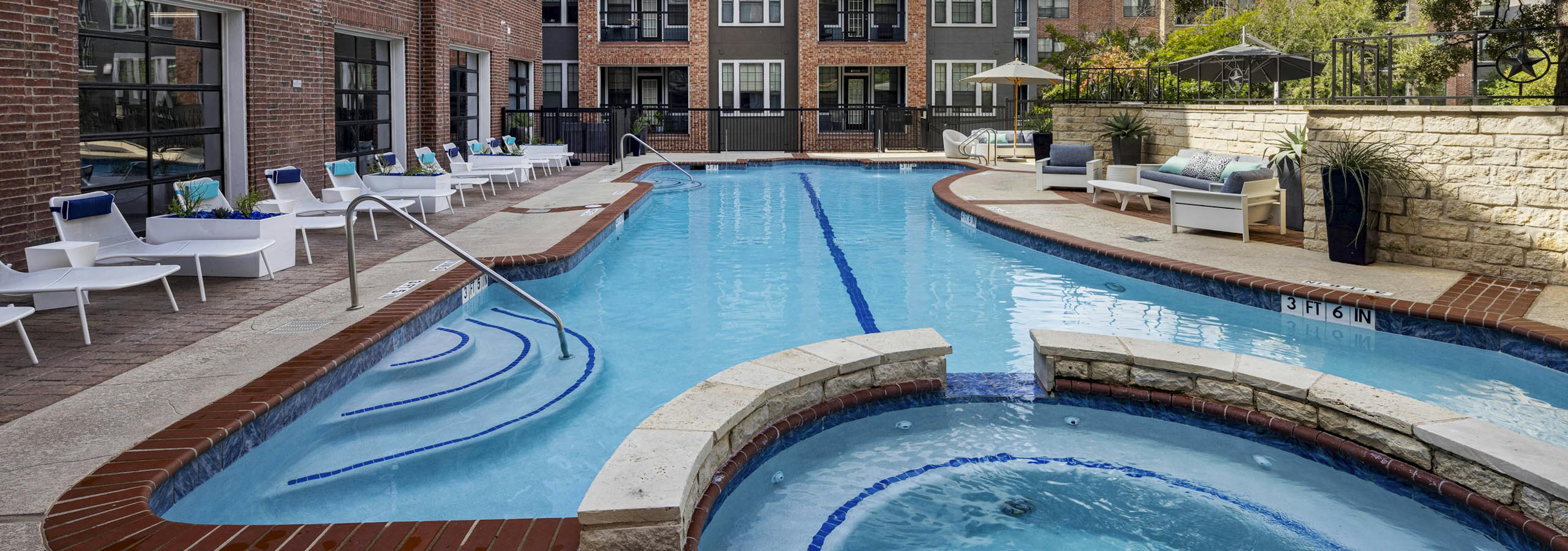AMLI Eastside apartments swimming pool with a connected circular hot tub surrounded by white lounge chairs and brick buildings