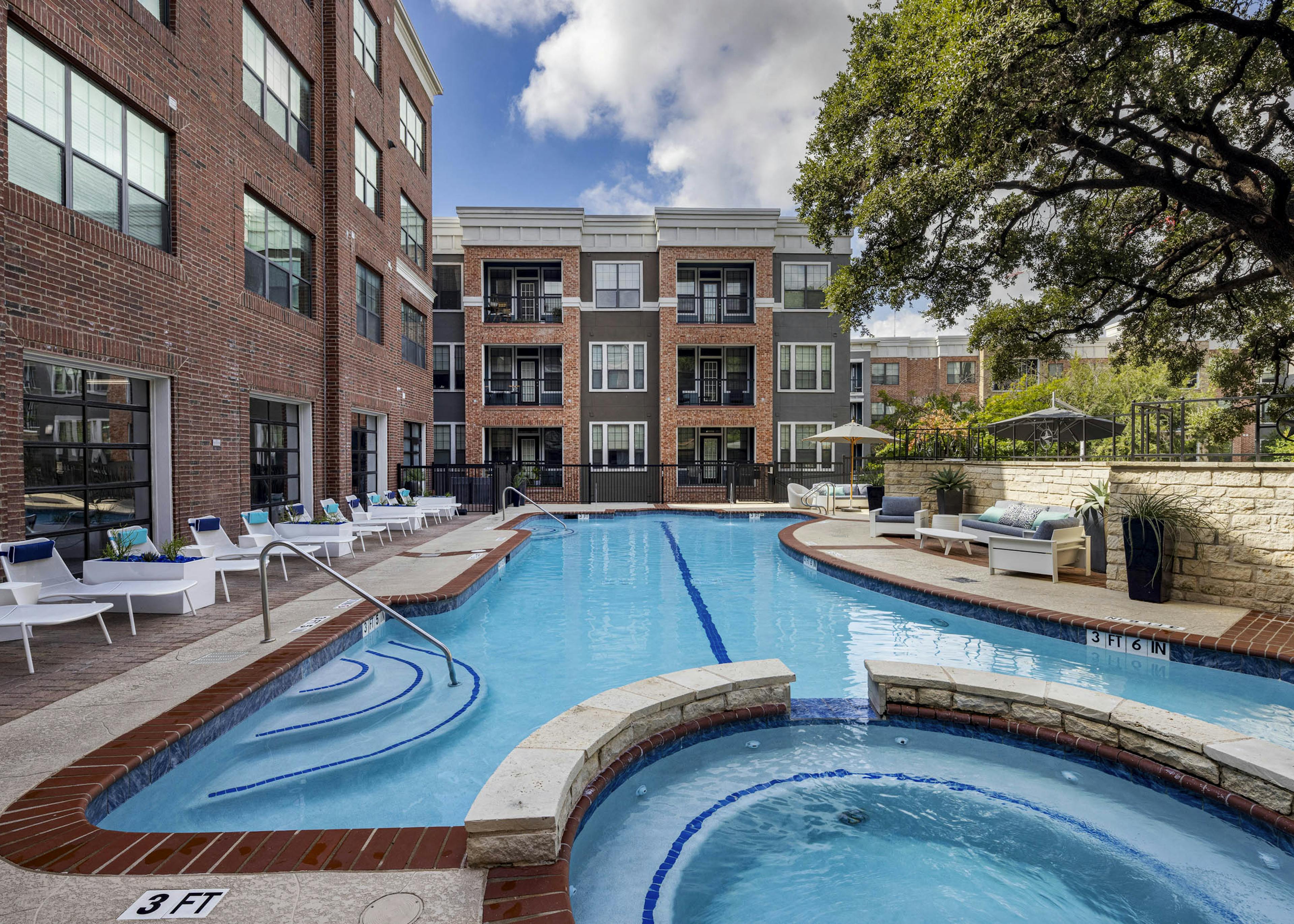 AMLI Eastside apartments swimming pool with a connected circular hot tub surrounded by white lounge chairs and brick buildings