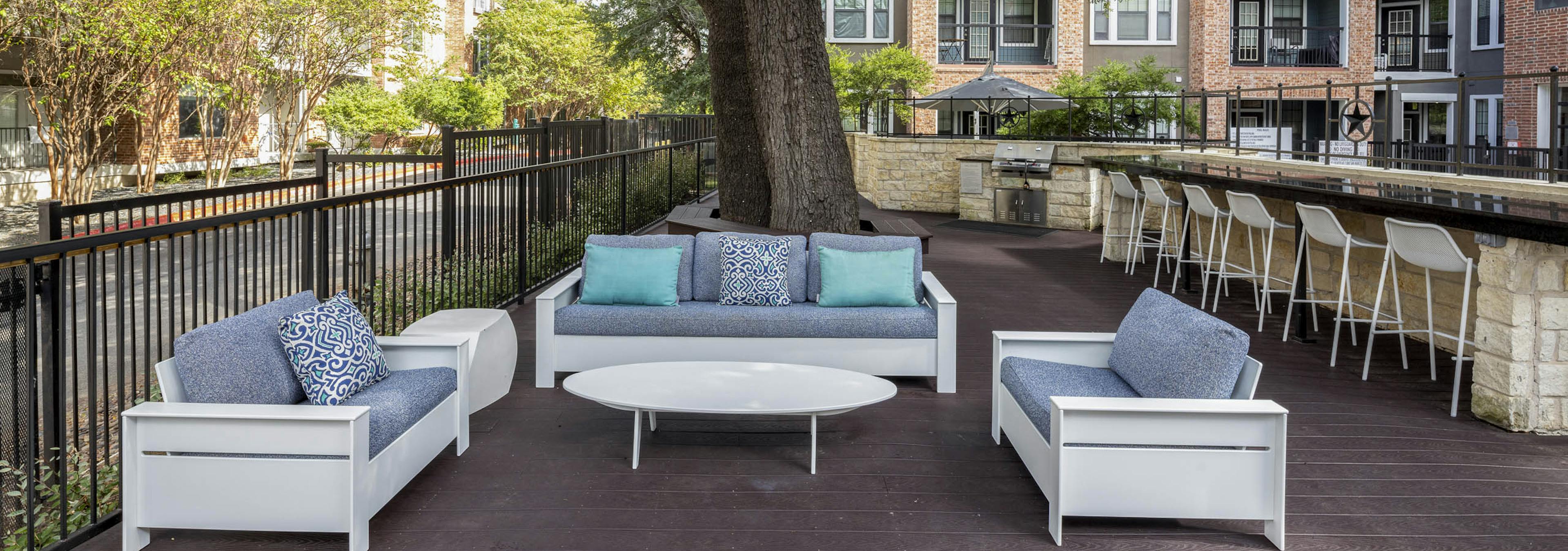Poolside grill deck at AMLI Eastside apartments with cushioned seating and a long counter with 7 white bar stools shaded by a large tree