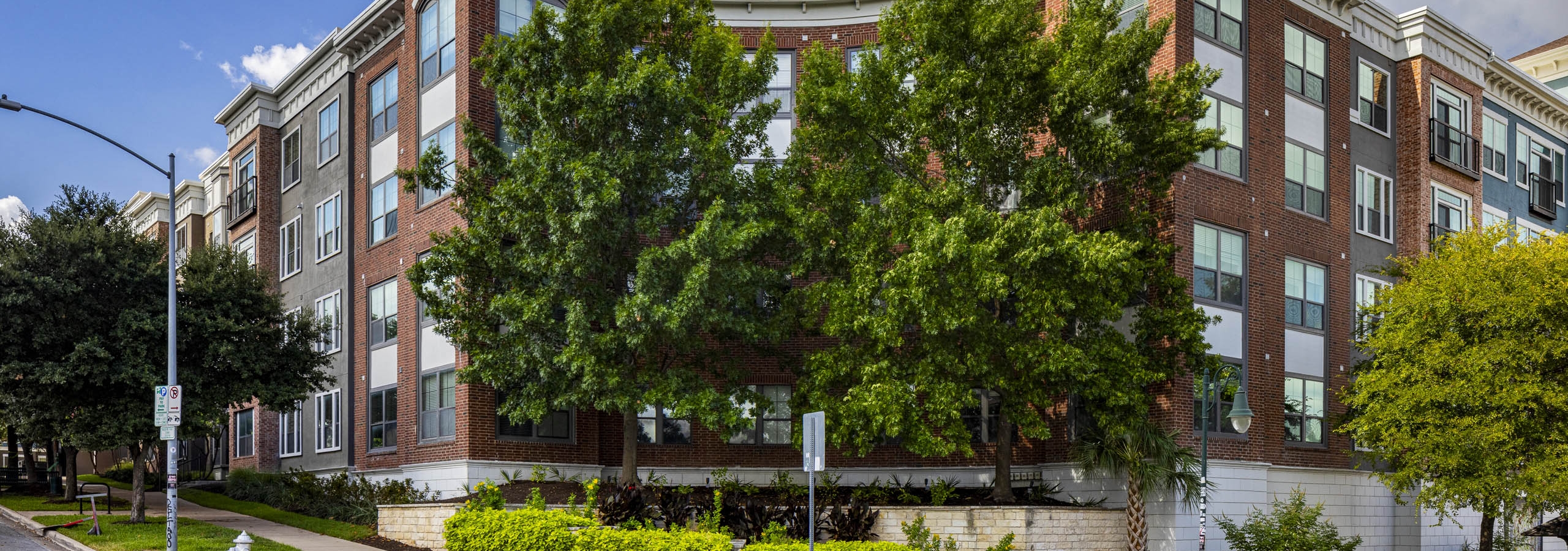 Daytime view of AMLI Eastside apartment building with red and white brick façade and surrounded by trees on a street corner