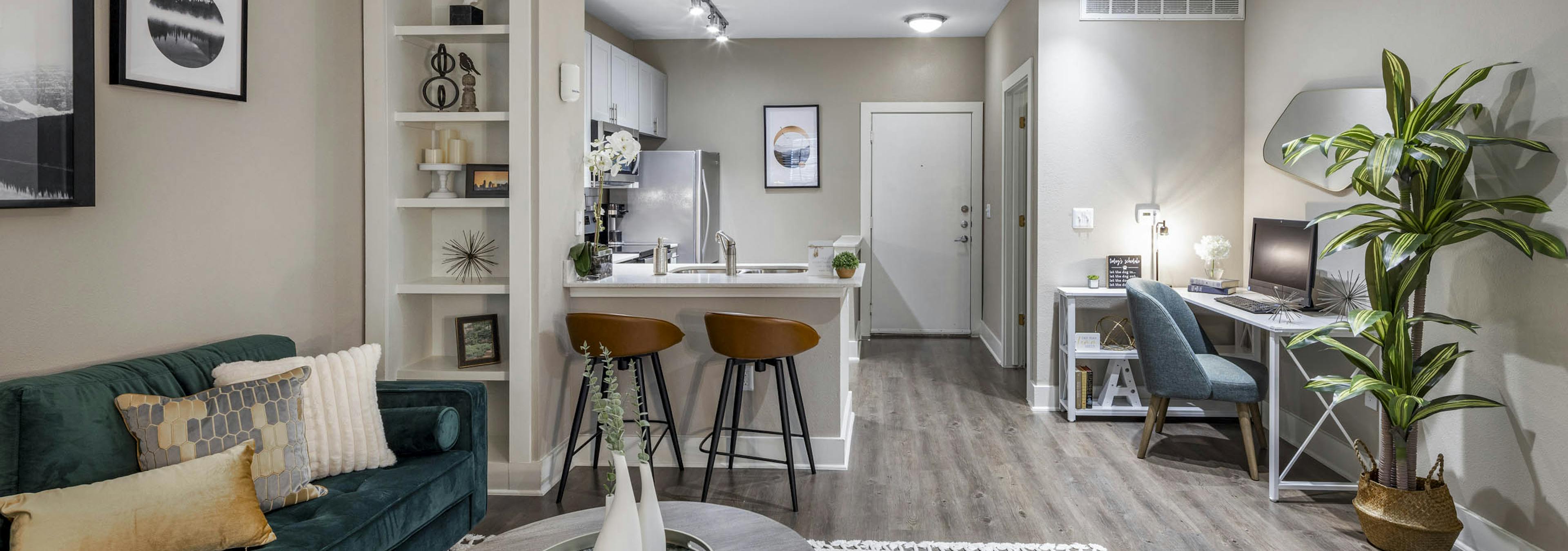 Fully furnished living room and kitchen at AMLI Eastside apartments boasting a built-in bookshelf, counter with 2 stools and a desk with chair