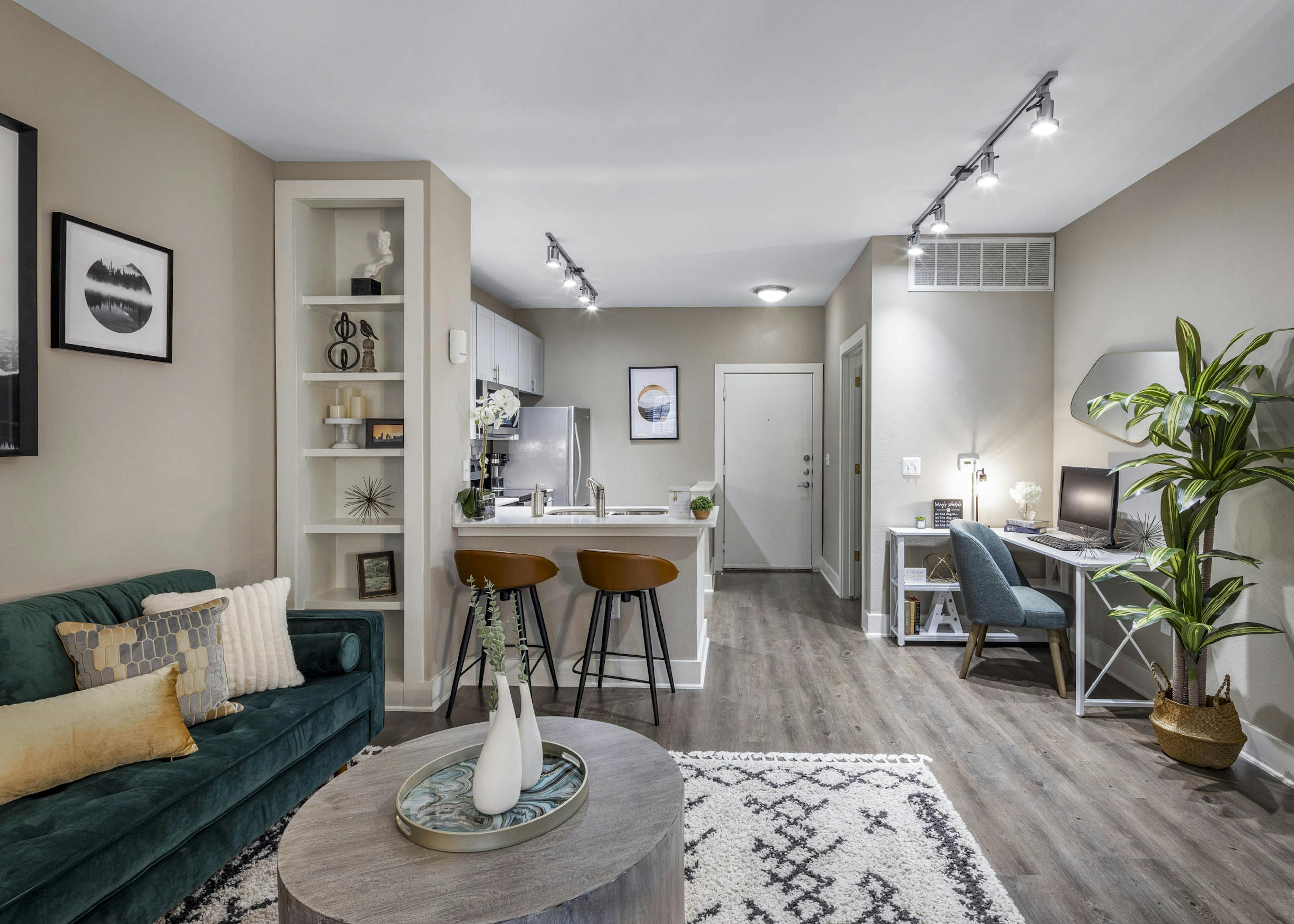 Fully furnished living room and kitchen at AMLI Eastside apartments boasting a built-in bookshelf, counter with 2 stools and a desk with chair