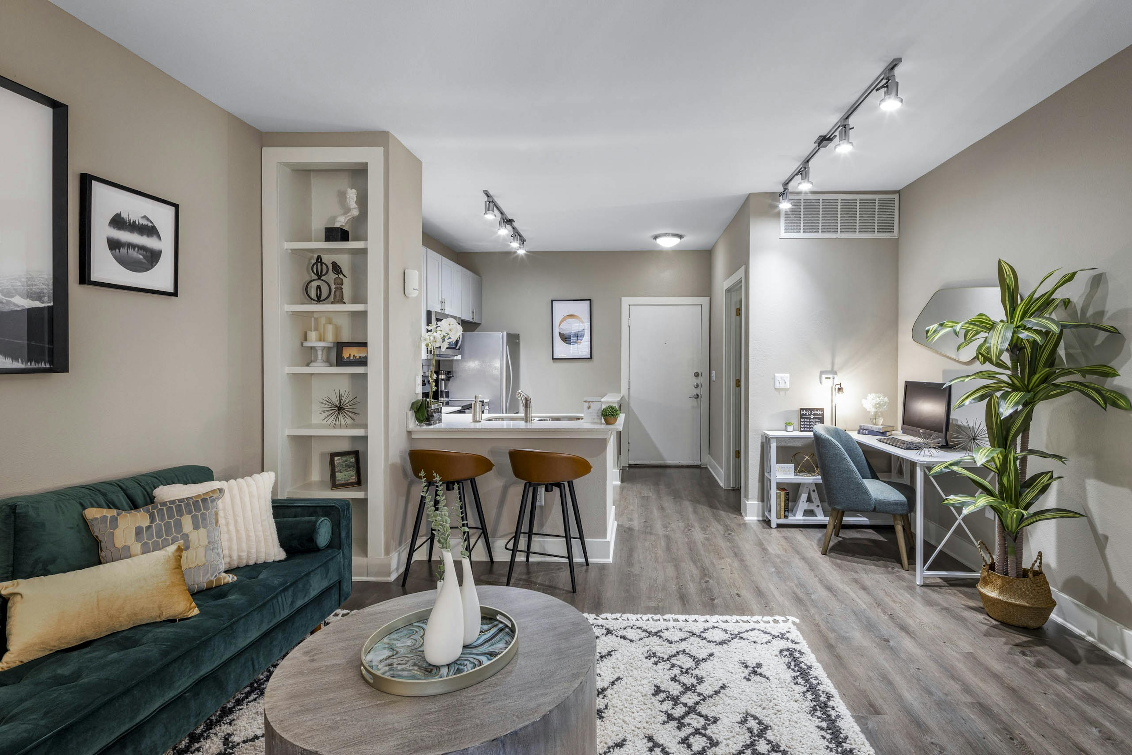Fully furnished living room and kitchen at AMLI Eastside apartments boasting a built-in bookshelf, counter with 2 stools and a desk with chair