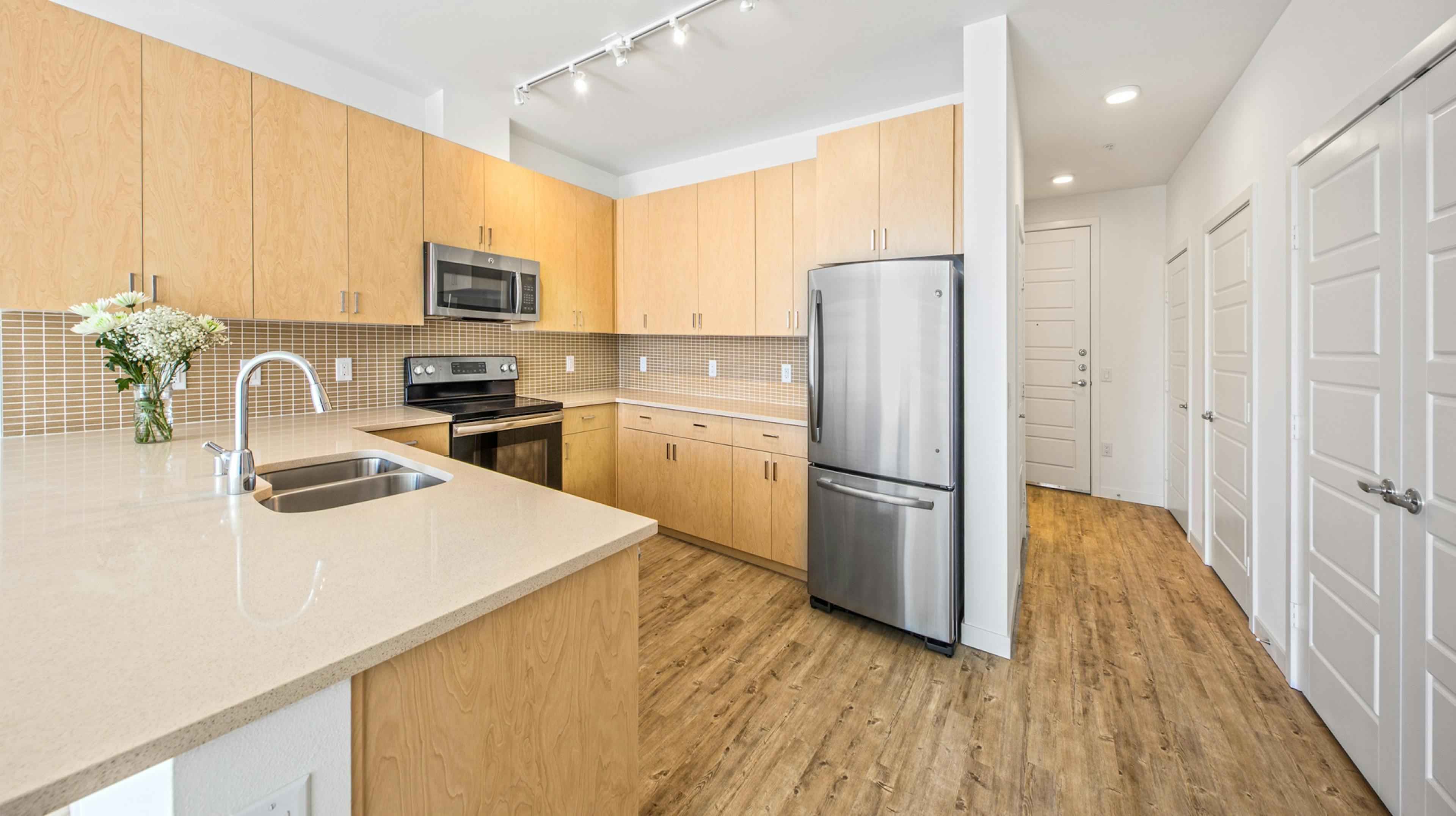 Interior view of an AMLI Wallingford apartment kitchen with light cabinets tan quartz counter tops and stainless steel appliances  