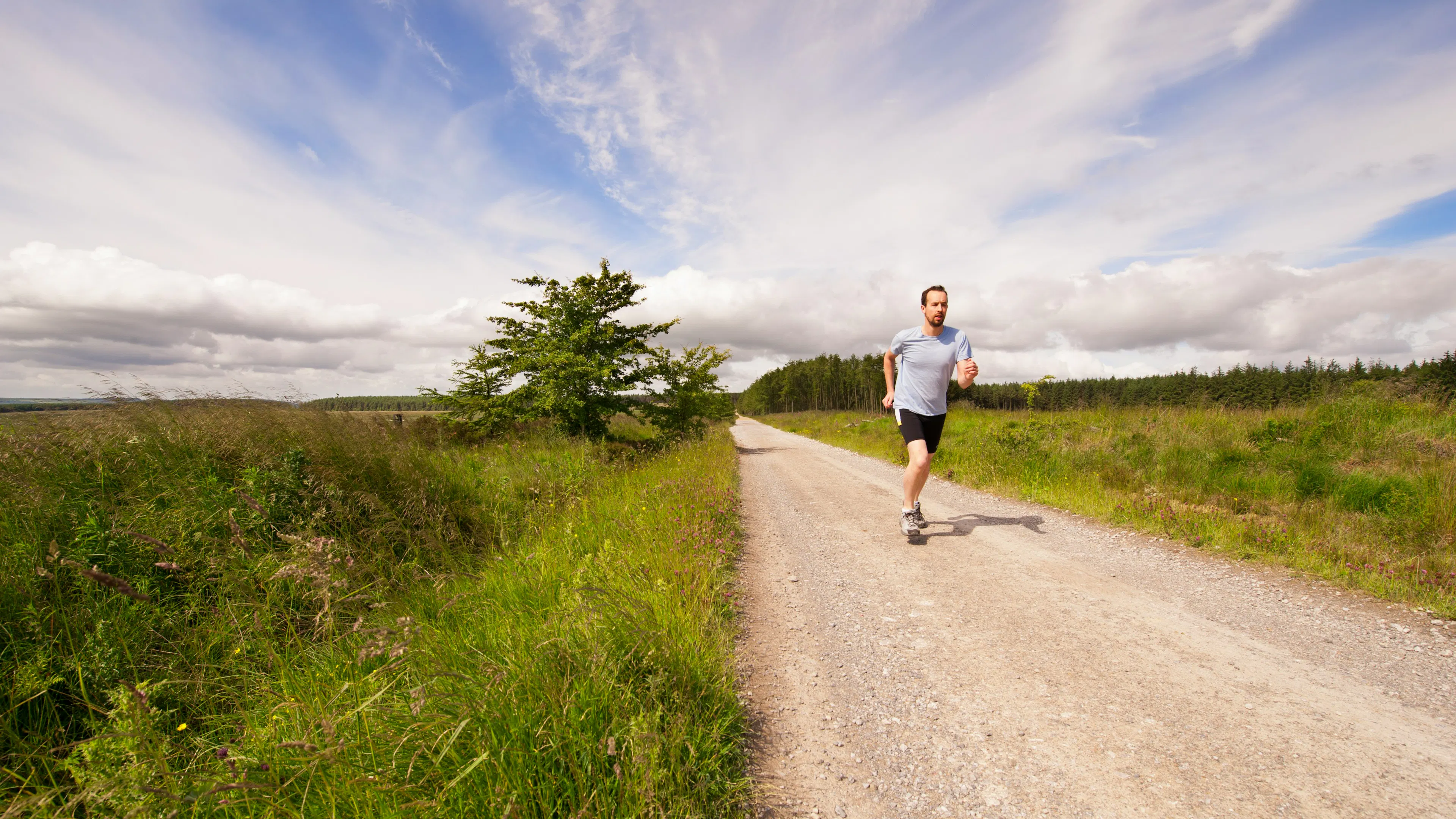 A man running down a long straight gravel trail on a sunny day