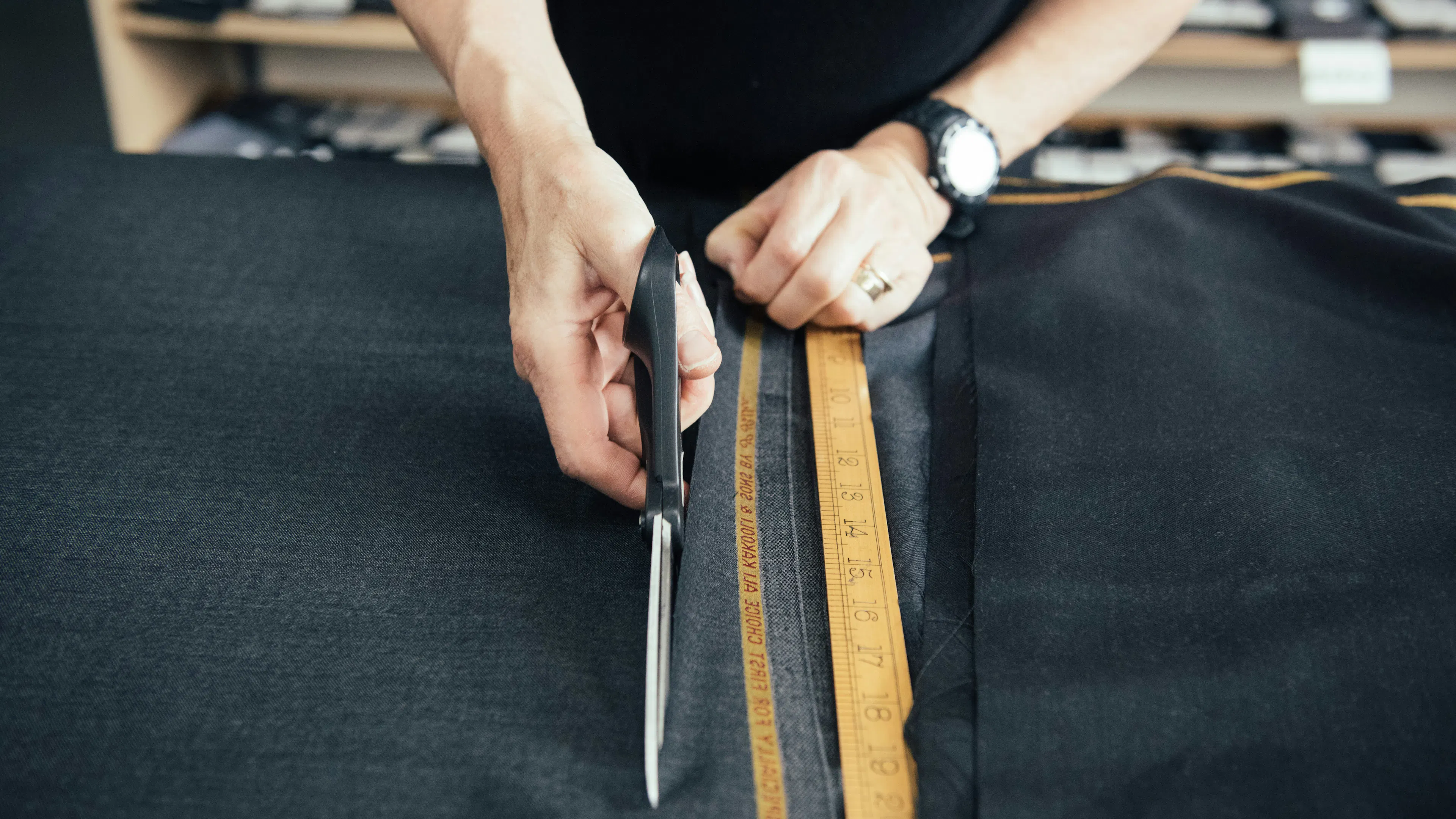 A person slicing a pair of scissors through some dark fabric on a wooden table