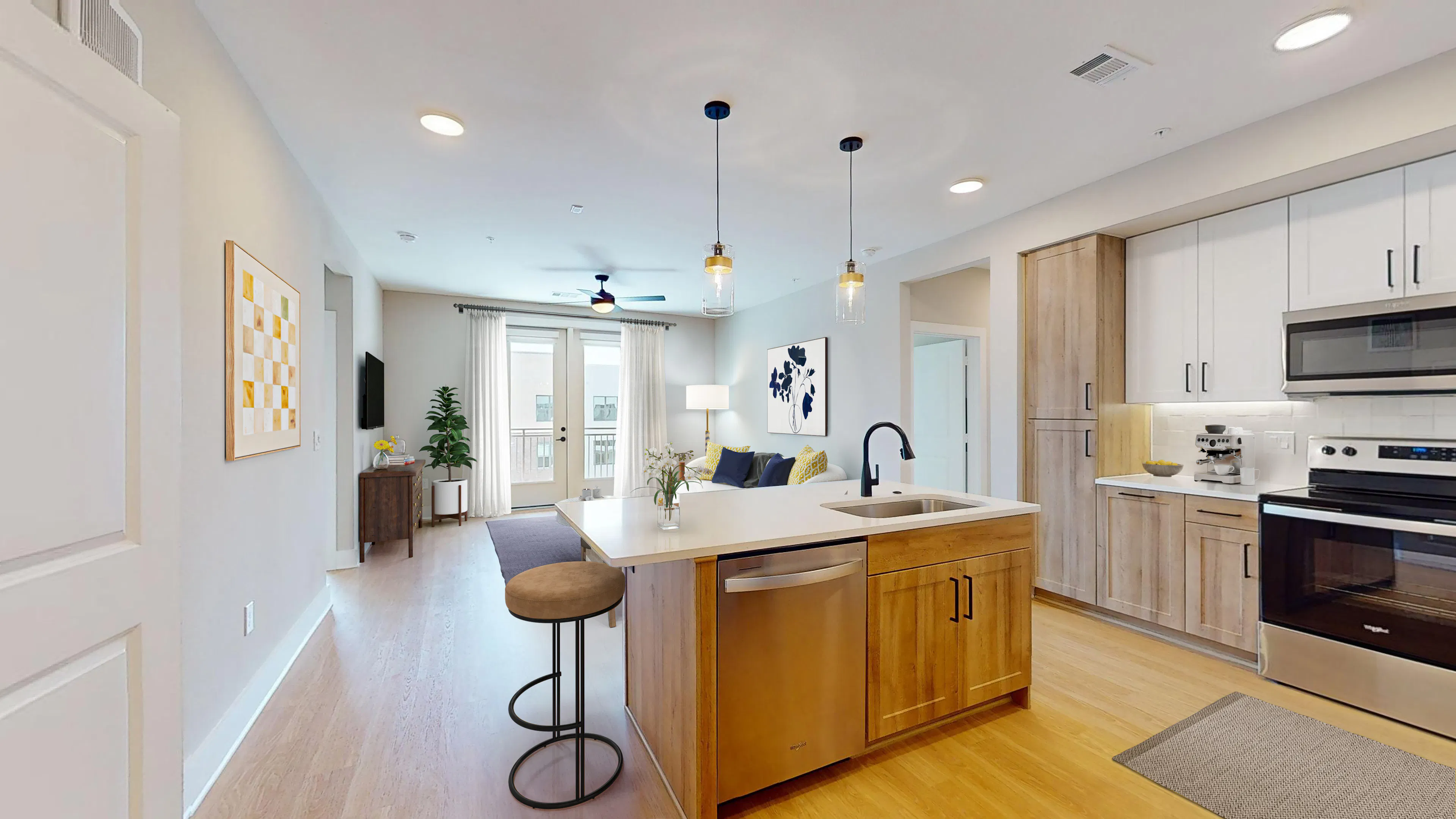 A well lit apartment interior with a kitchen island leading into a living room with a balcony leading outdoors