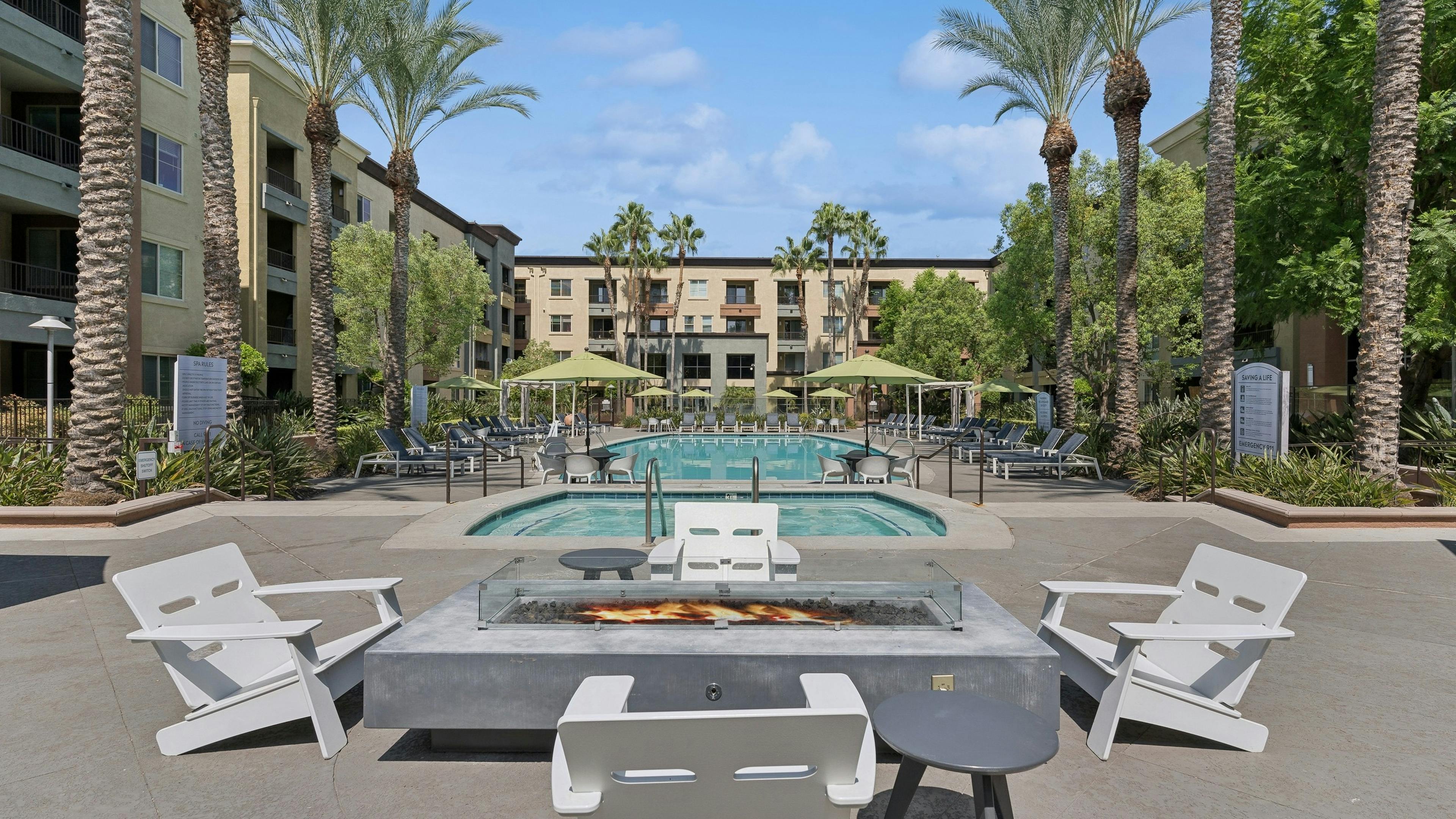 Daytime view of AMLI Warner Center courtyard with gray fire table surrounded by 4 white chairs with view of pool and spa