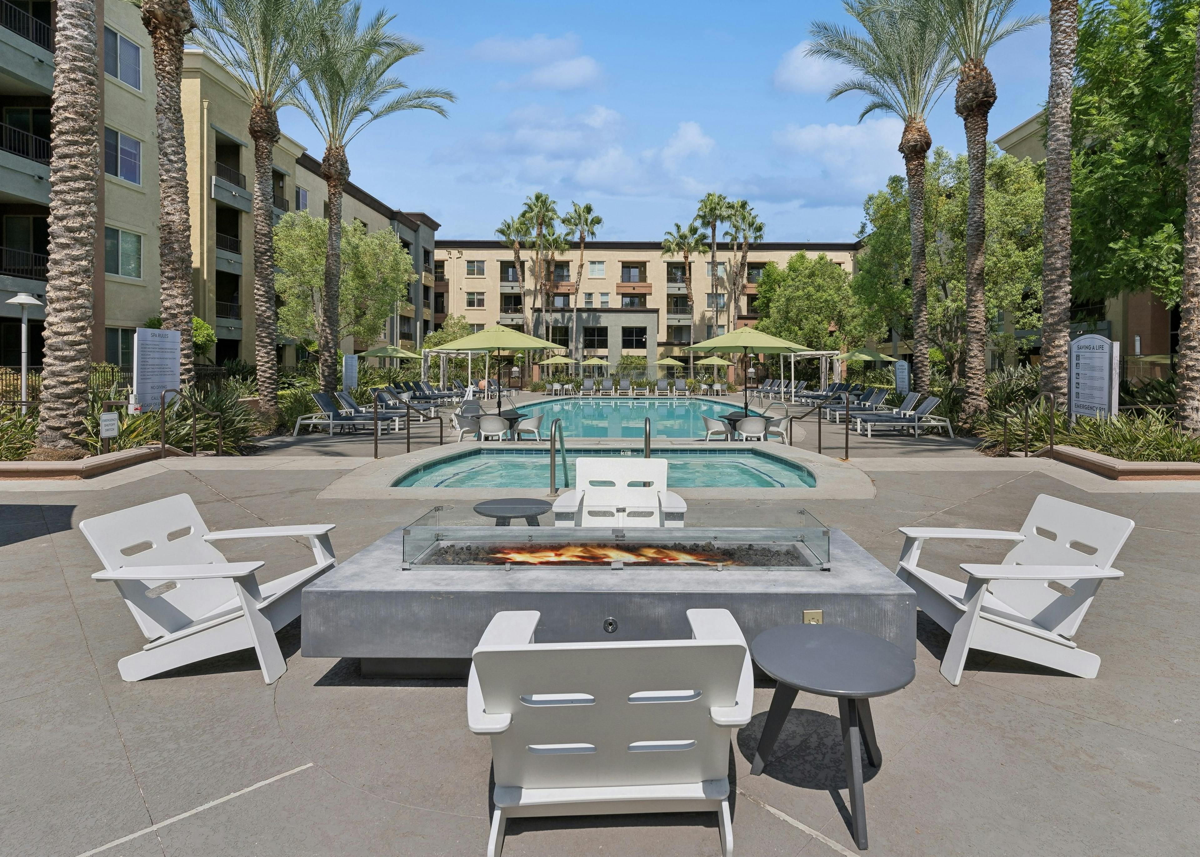 Daytime view of AMLI Warner Center courtyard with gray fire table surrounded by 4 white chairs with view of pool and spa