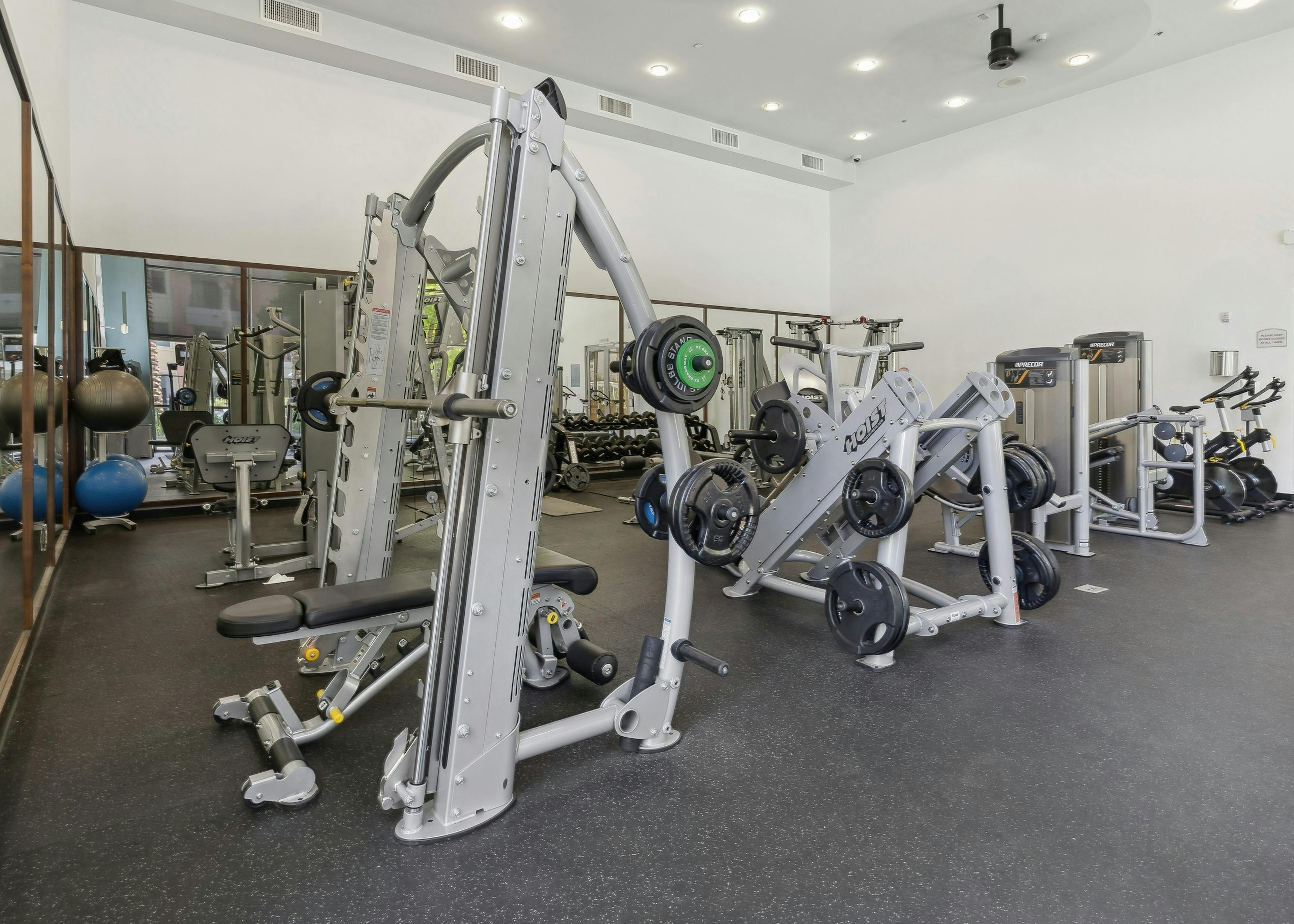 The fitness center at AMLI Warner Center showcases a Smith machine, weight racks, several cardio machines and 2 large mirrored walls