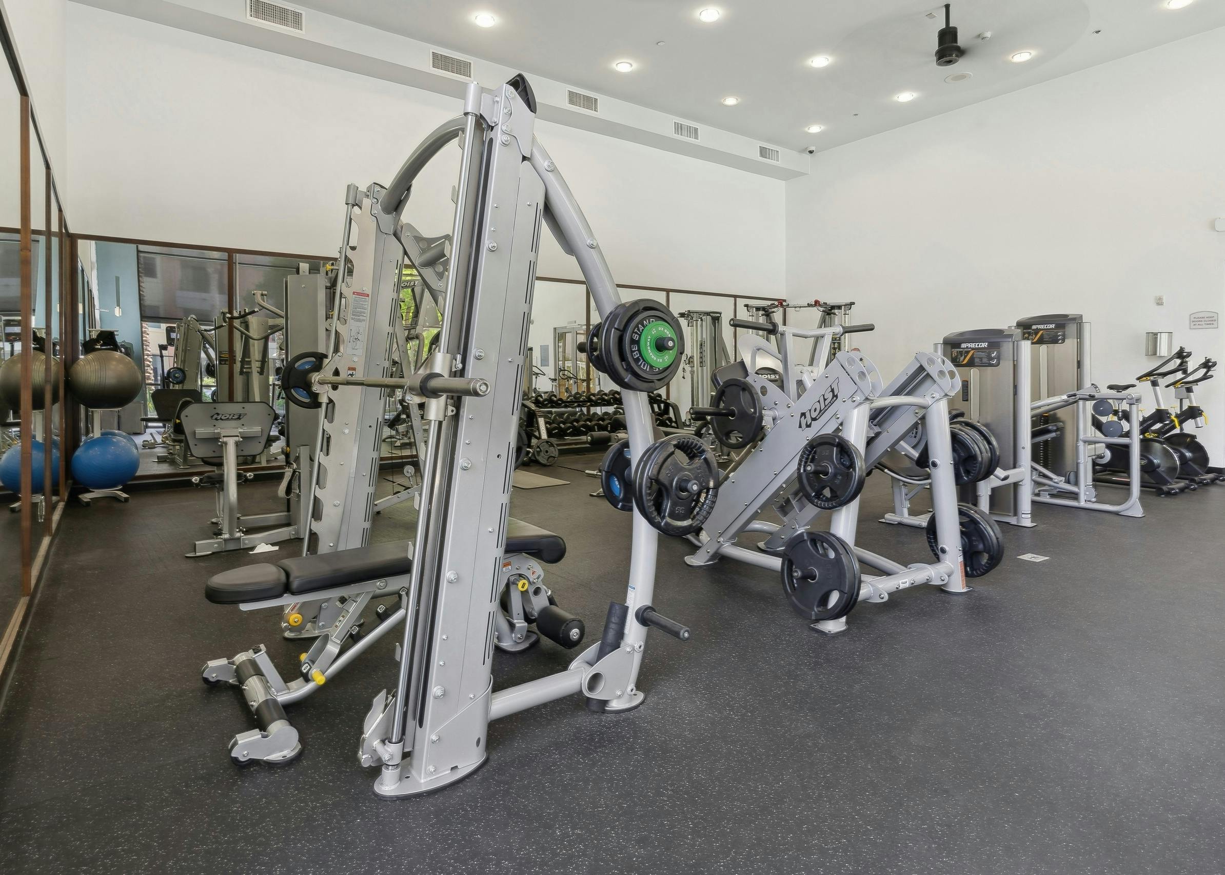 The fitness center at AMLI Warner Center showcases a Smith machine, weight racks, several cardio machines and 2 large mirrored walls