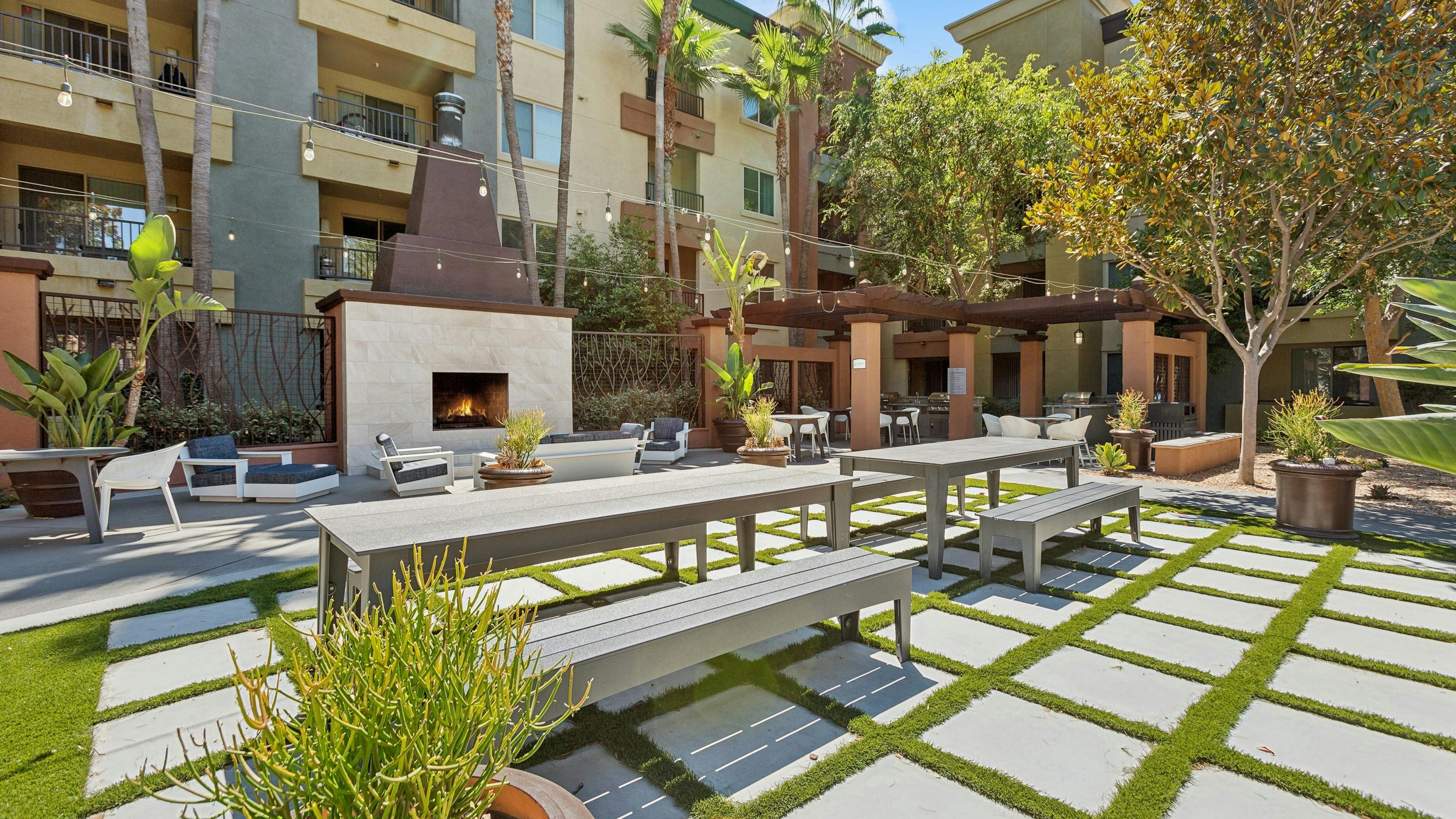 An outdoor community area at AMLI Warner Center featuring a fireplace surrounded by lounge seating and a grid of stone pavers with grass
