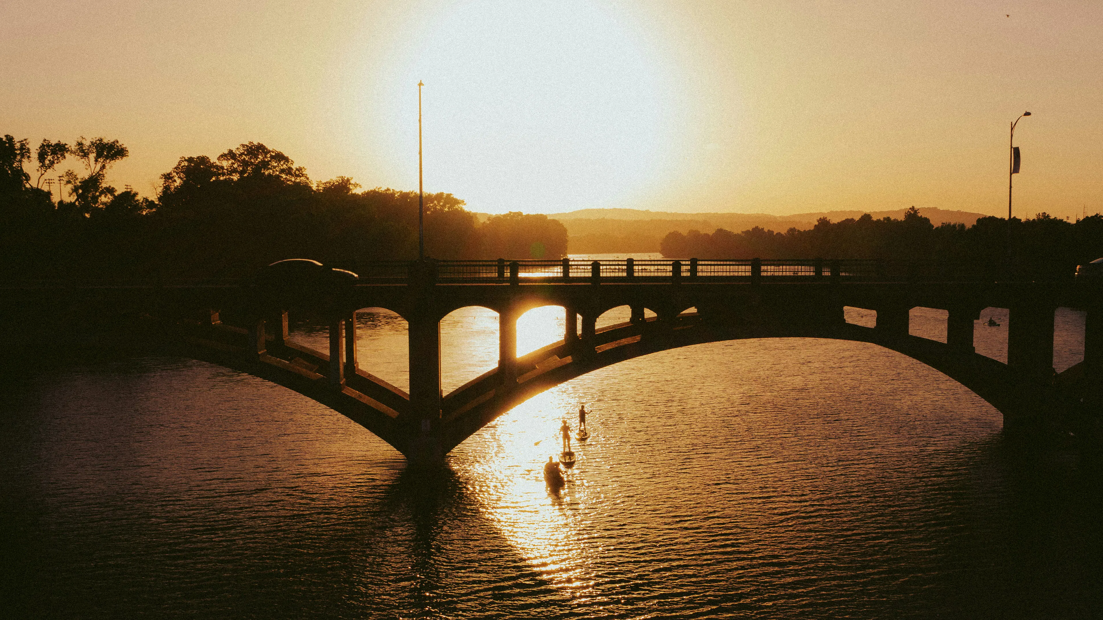 The silhouette of Austin's Congress Avenue Bridge with paddle boarders floating underneath at sunset