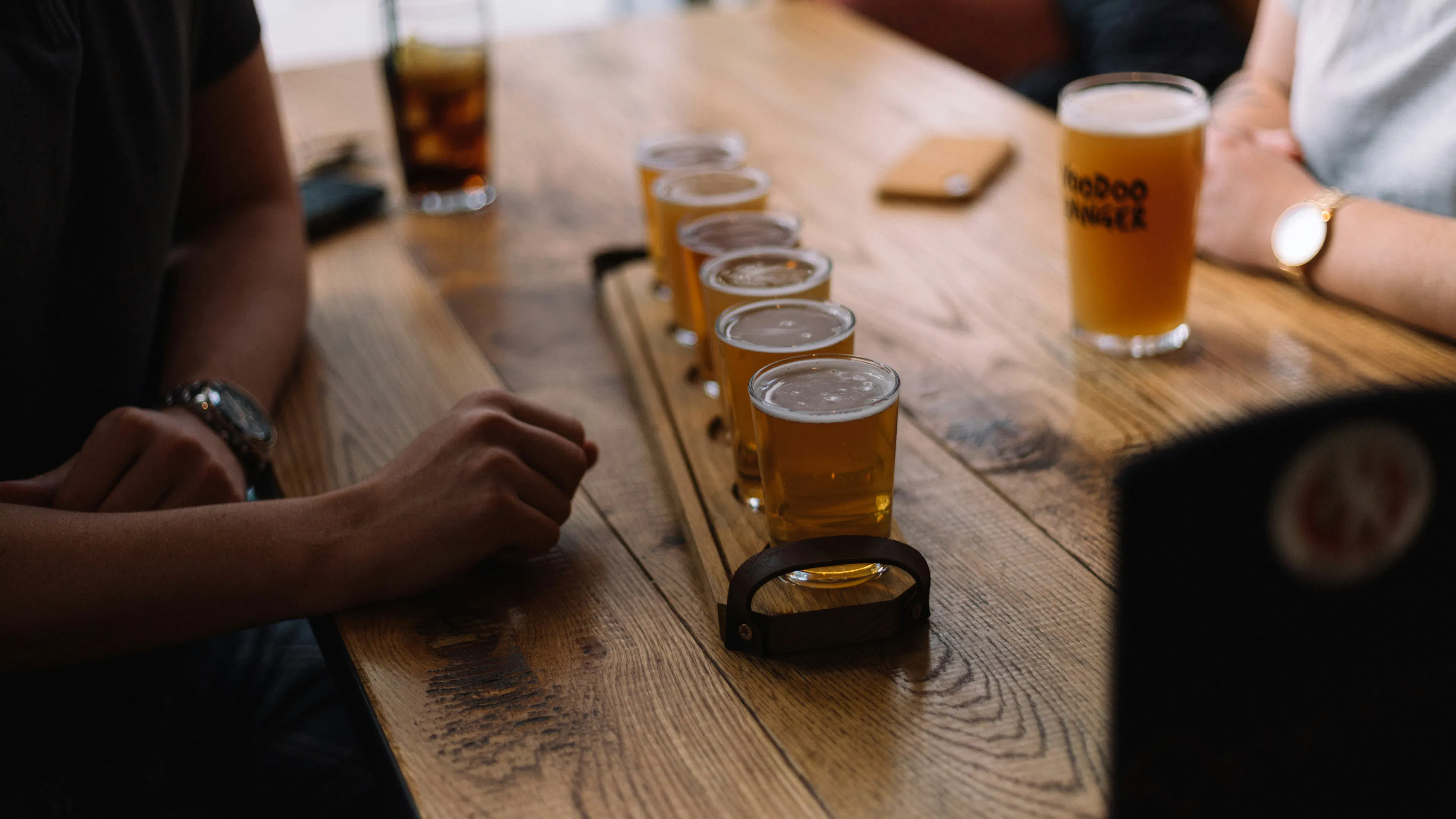 A flight of beer on a wooden table with three people around it
