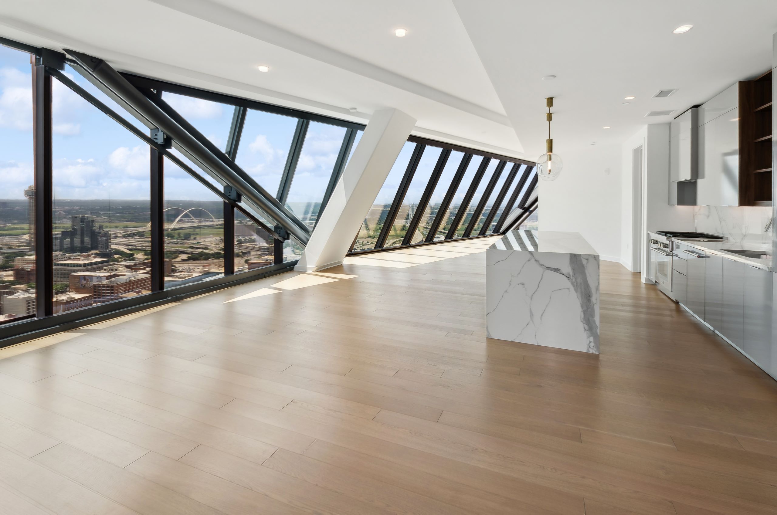 AMLI Fountain Place penthouse apartment living area and island kitchen with wood floors and floor to ceiling angled windows with city view