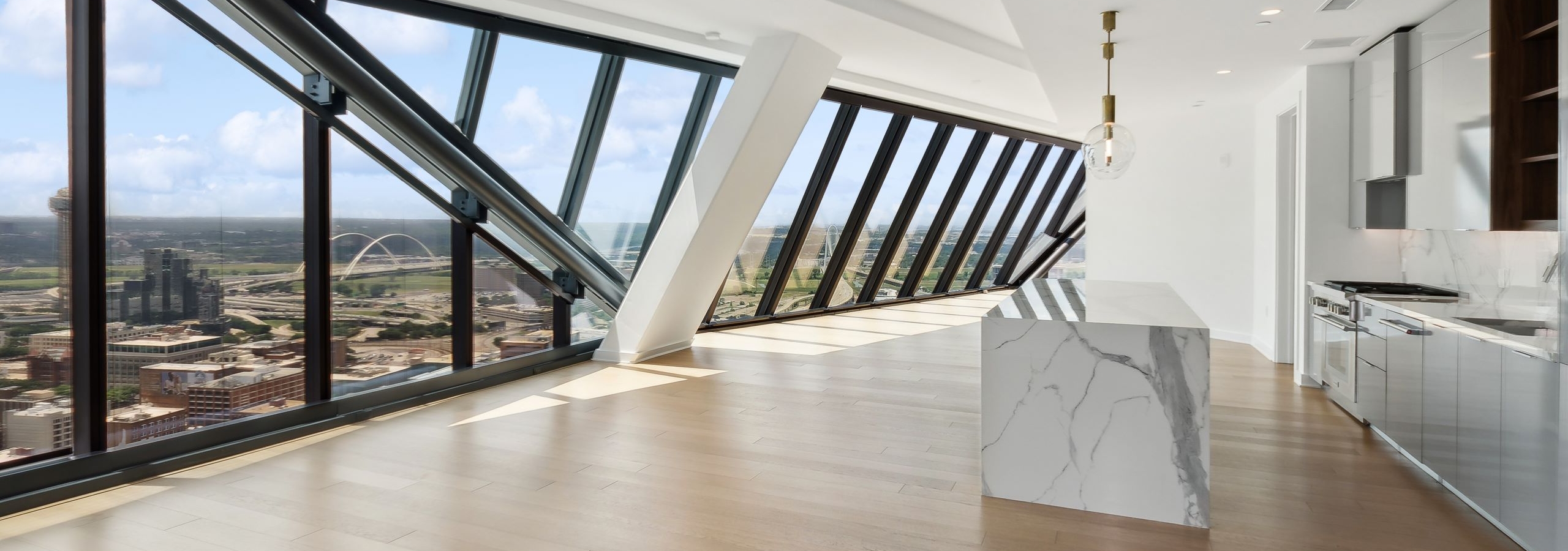 AMLI Fountain Place penthouse apartment living area and island kitchen with wood floors and floor to ceiling angled windows with city view