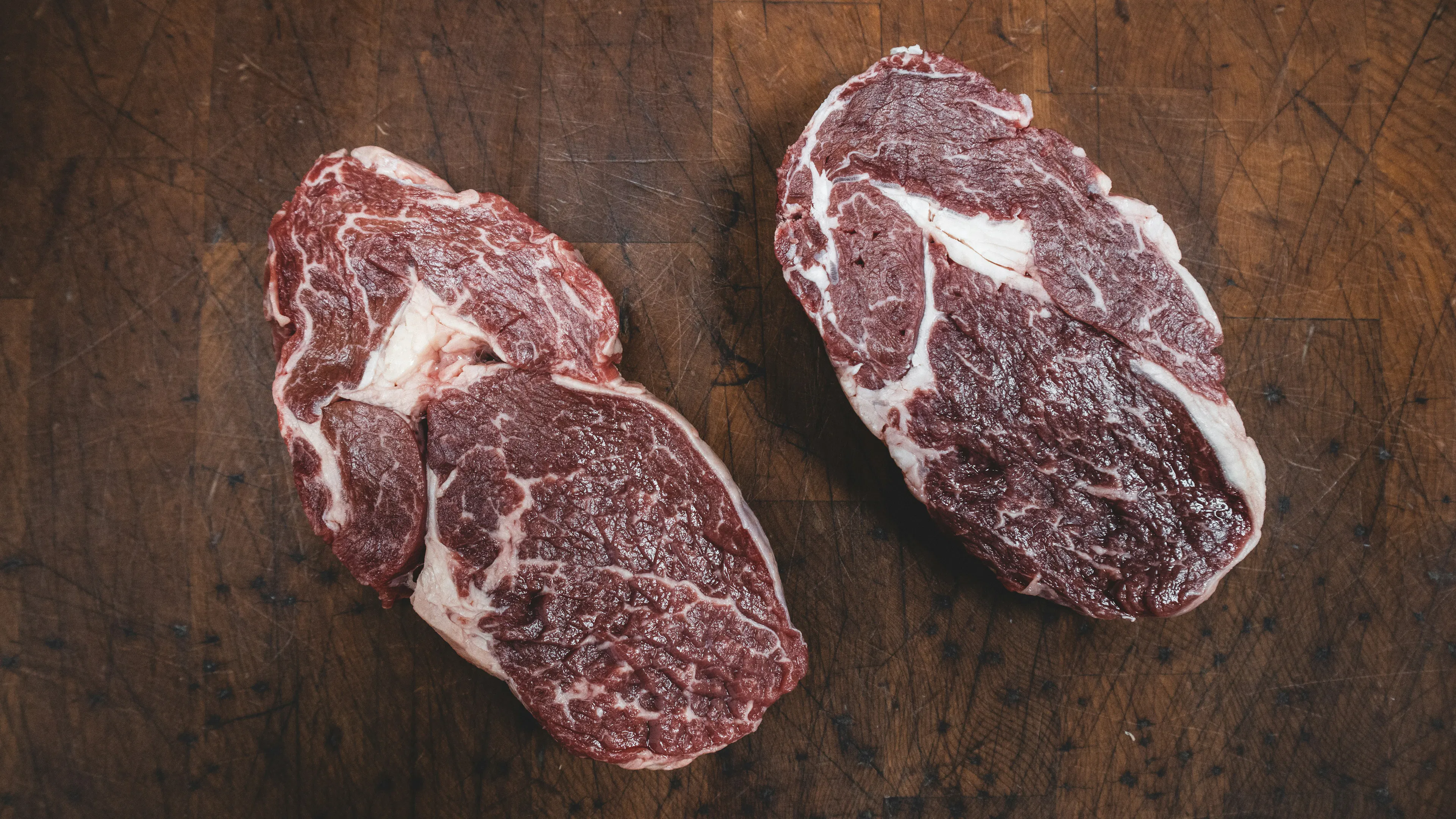 Two raw bison steaks resting on a wooden chopping block