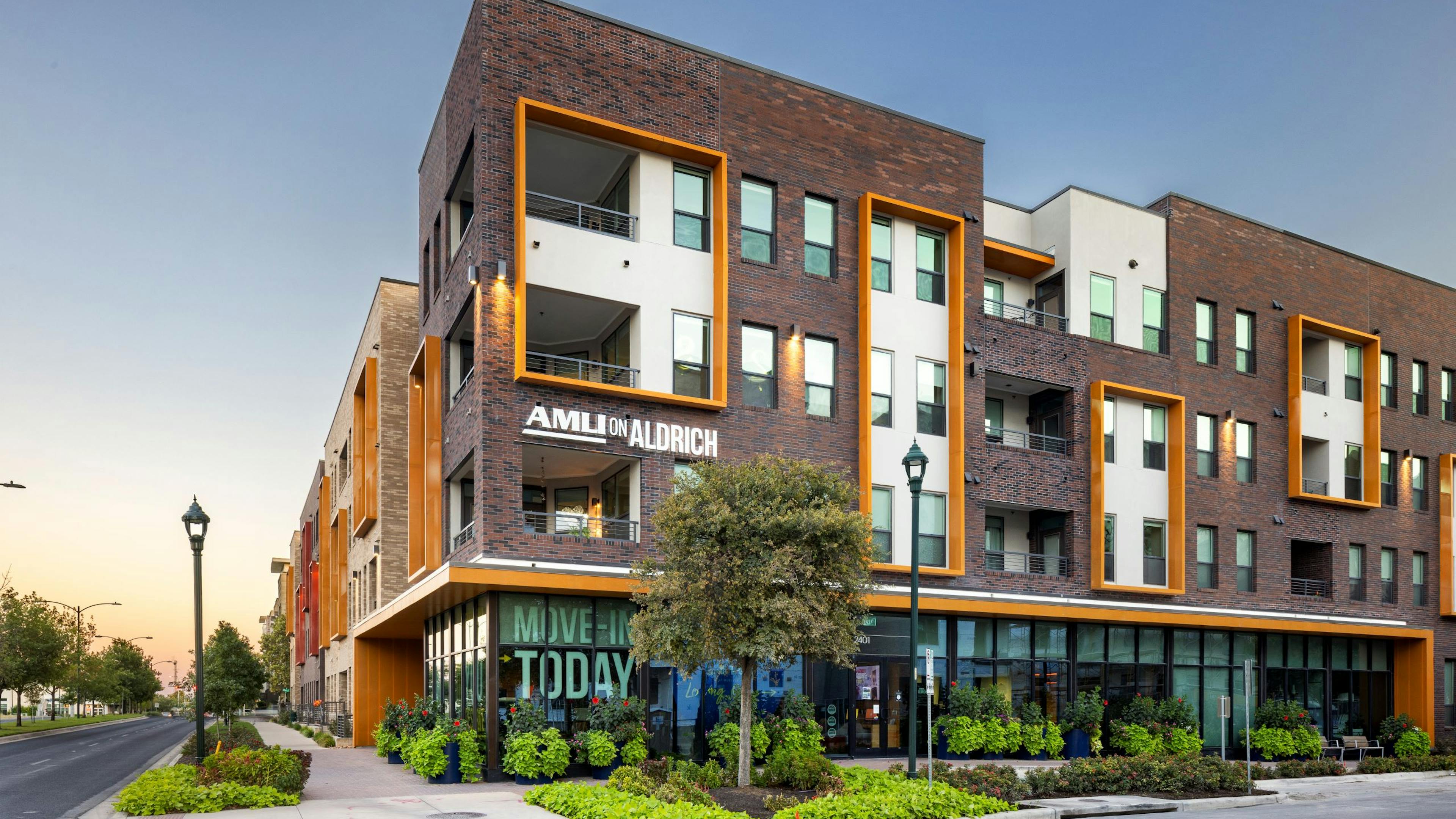 Exterior view of AMLI on Aldrich brick apartment building with large first floor windows amidst lush landscaping on a tree lined street.