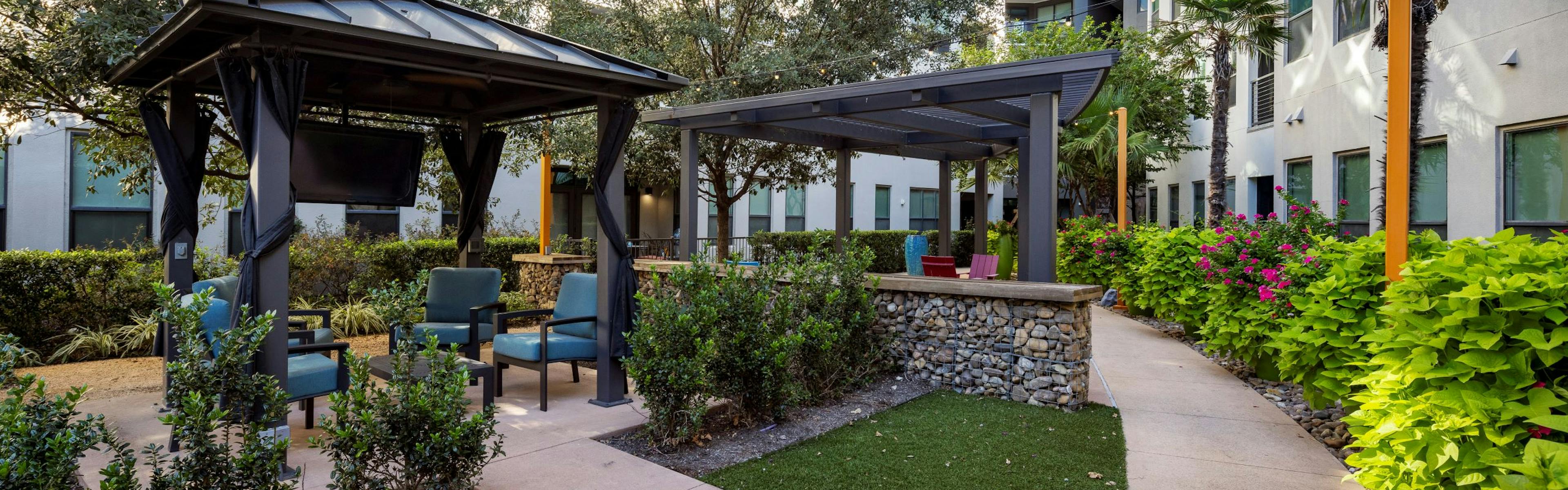 Day view of AMLI on Aldrich courtyard boasts lush greenery, two inviting pergolas with seating areas and a TV hanging beneath one.