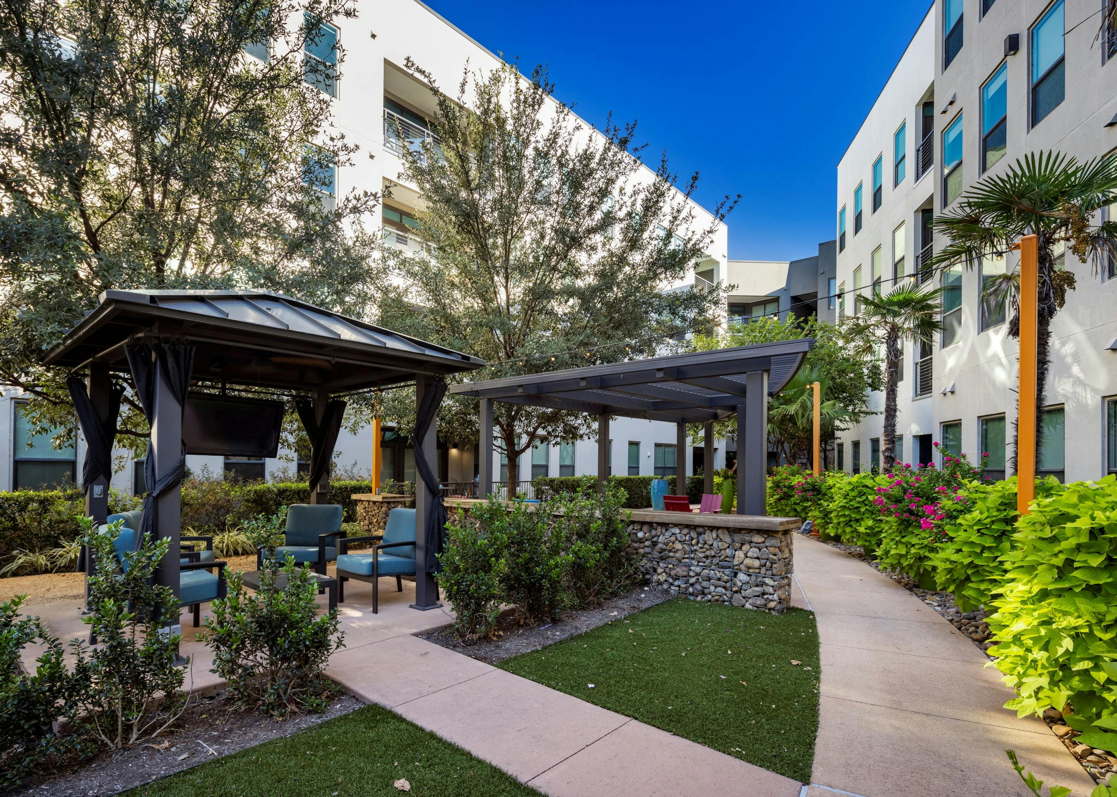 Day view of AMLI on Aldrich courtyard boasts lush greenery, two inviting pergolas with seating areas and a TV hanging beneath one.
