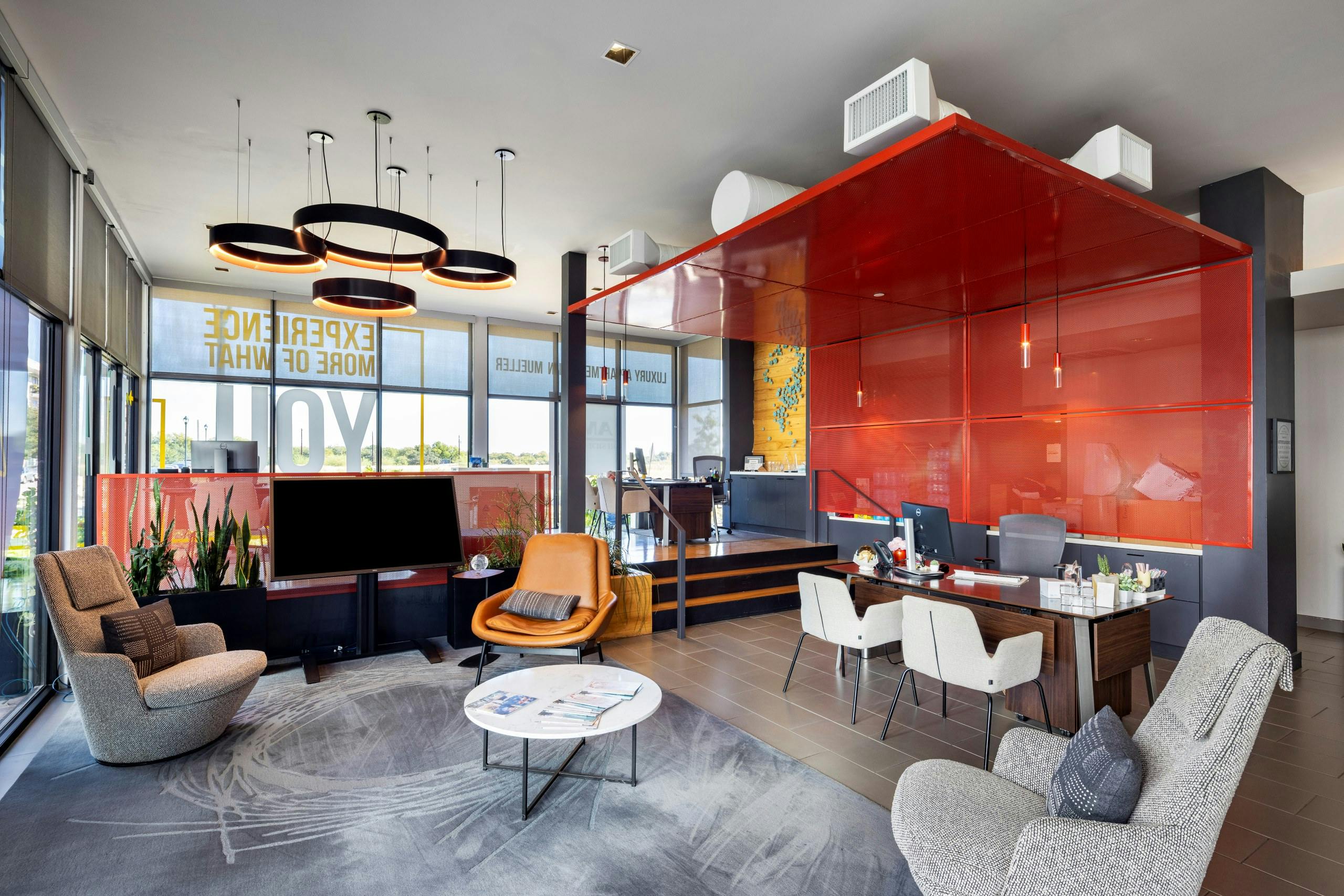 Leasing office at AMLI on Aldrich apartments with orange and gray décor, desks, comfortable chairs, and a flat screen TV and large windows.